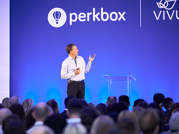 A speaker presenting to a seated audience beneath Perkbox and Vivup branding at a conference