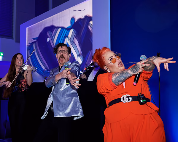 Vocalists and a violinist performing on stage in bright outfits at a corporate party