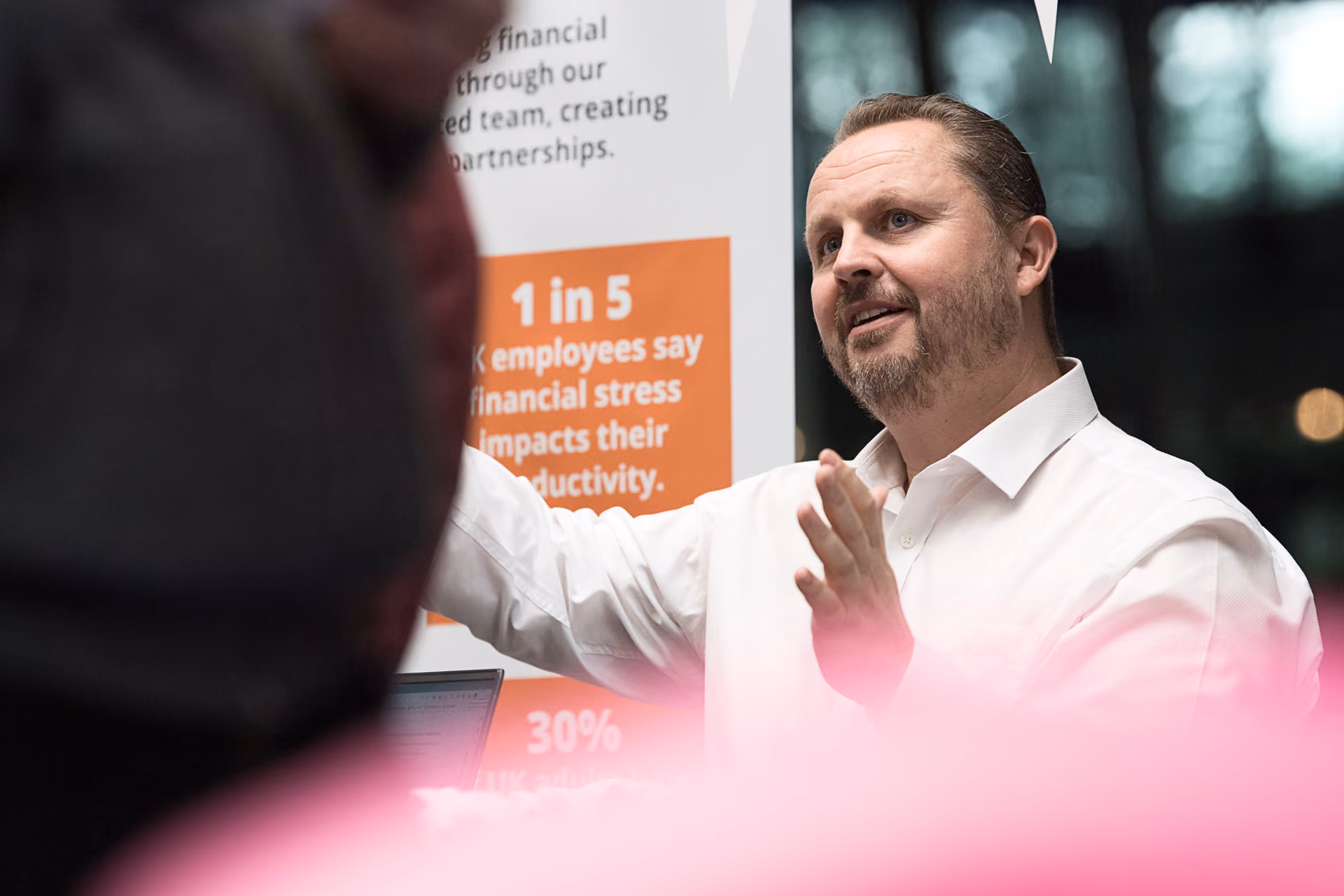 An exhibitor speaking to visitors beside a financial wellbeing banner at a corporate event