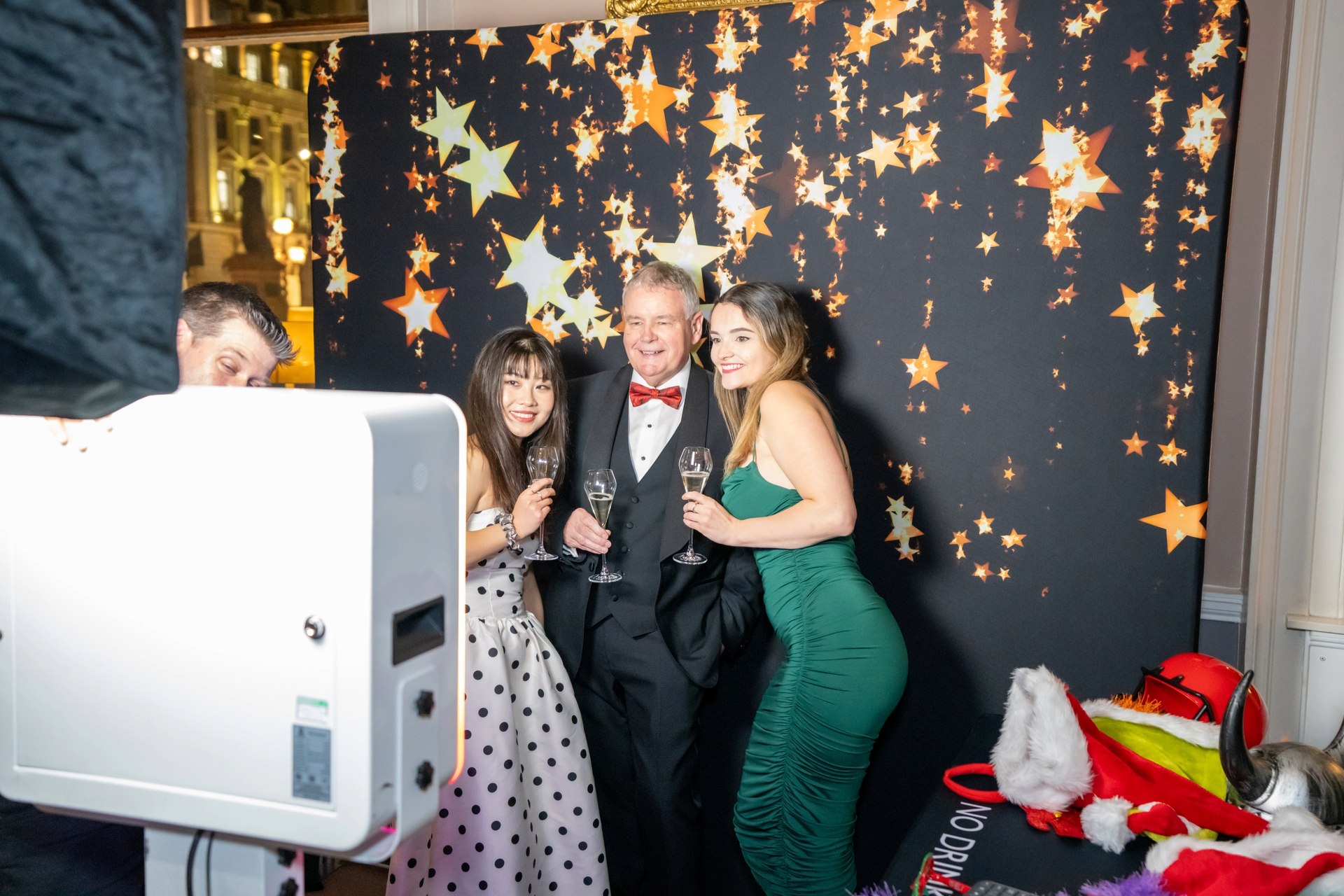 Three guests posing with drinks in a photo booth against a gold star backdrop