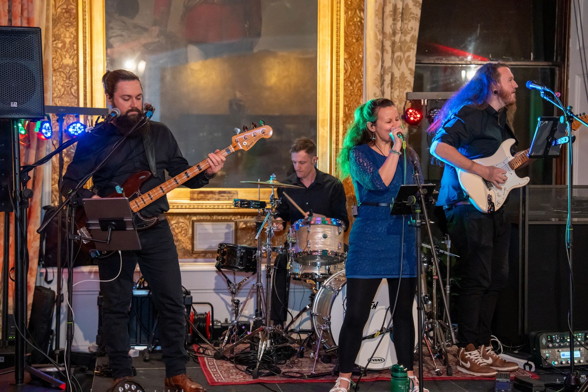 A four-piece live band performing on stage in an ornate panelled function room