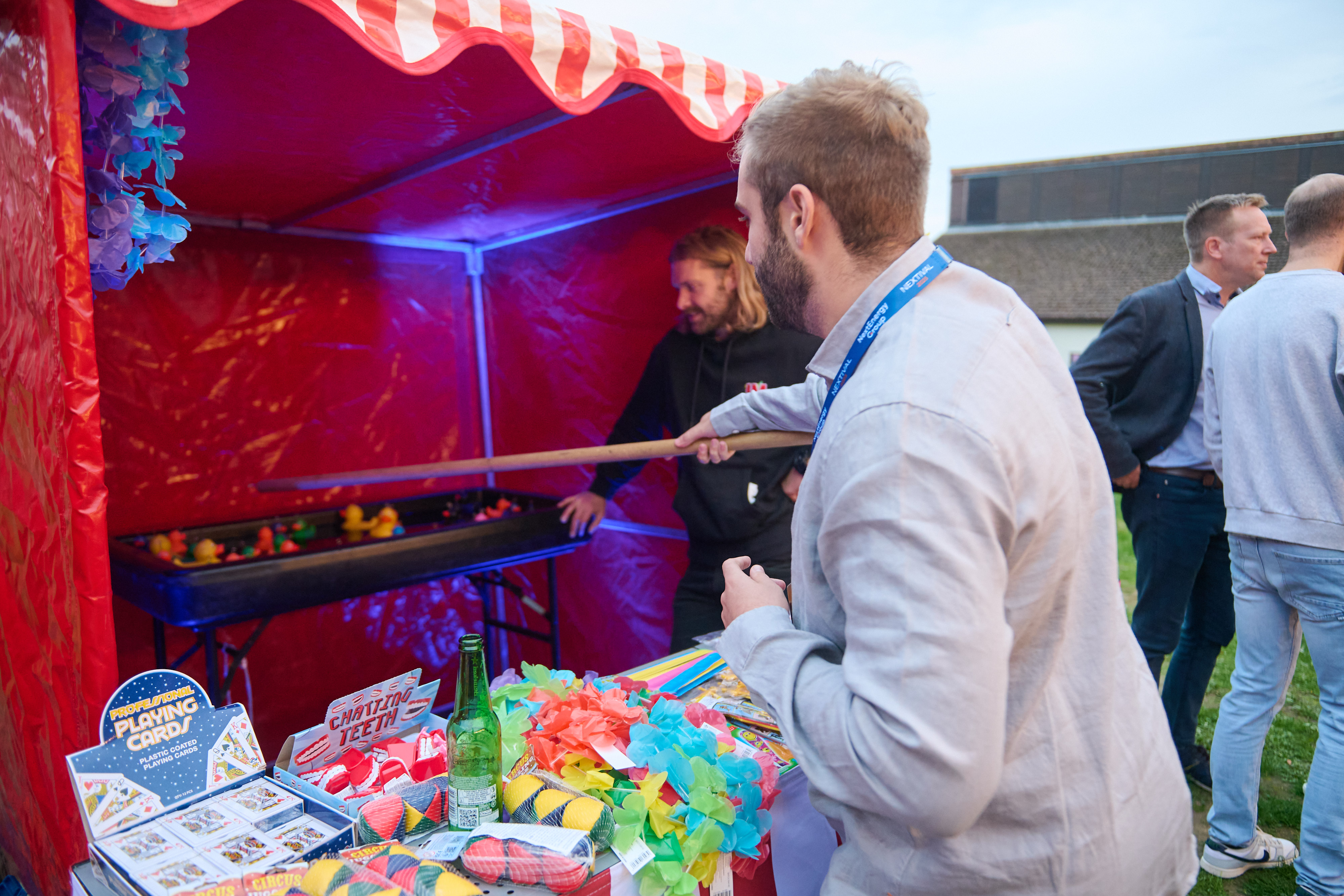 A man playing a hook-a-duck fairground stall under a red and white canopy
