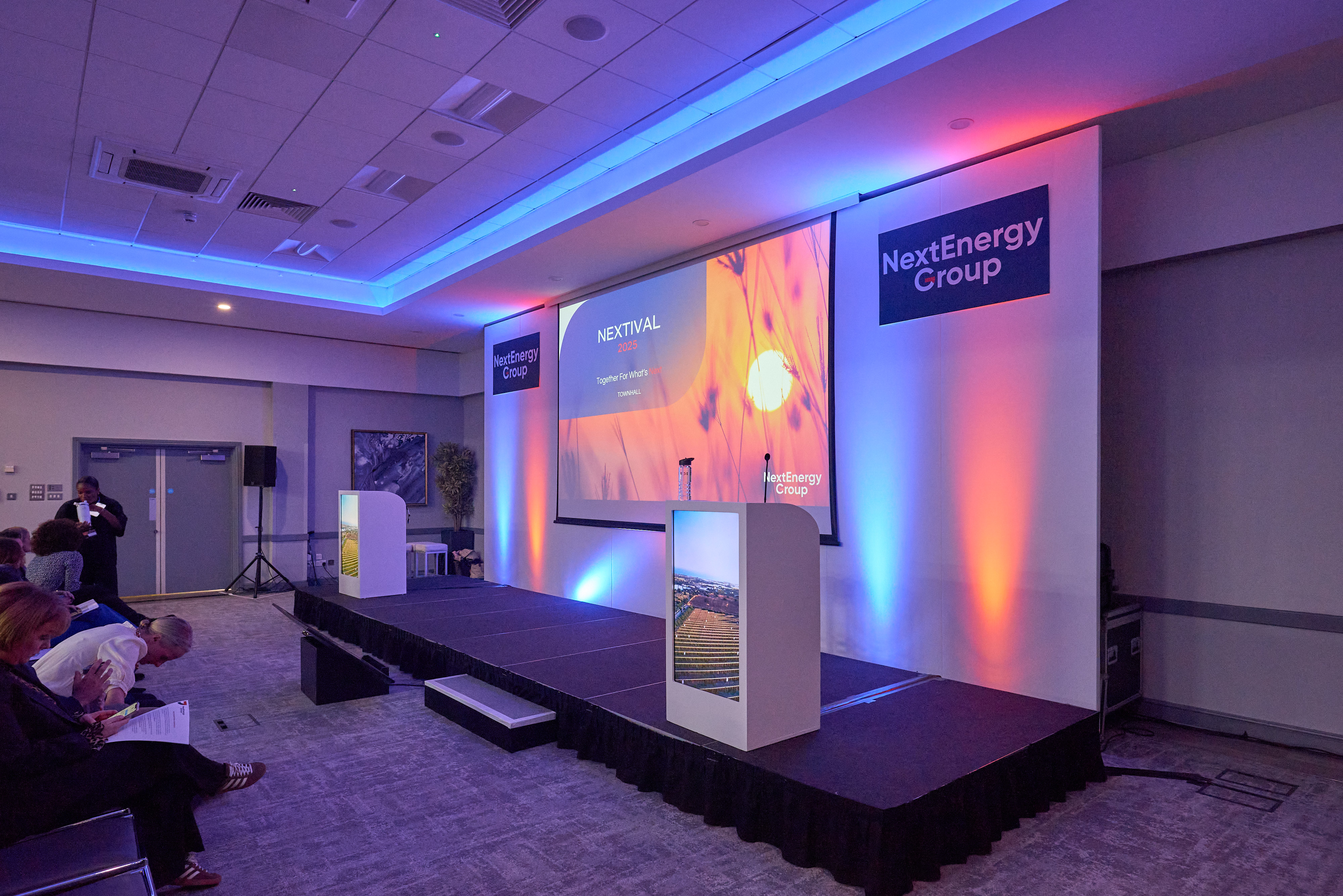 An empty stage set with a lectern and screens before a company all-hands session