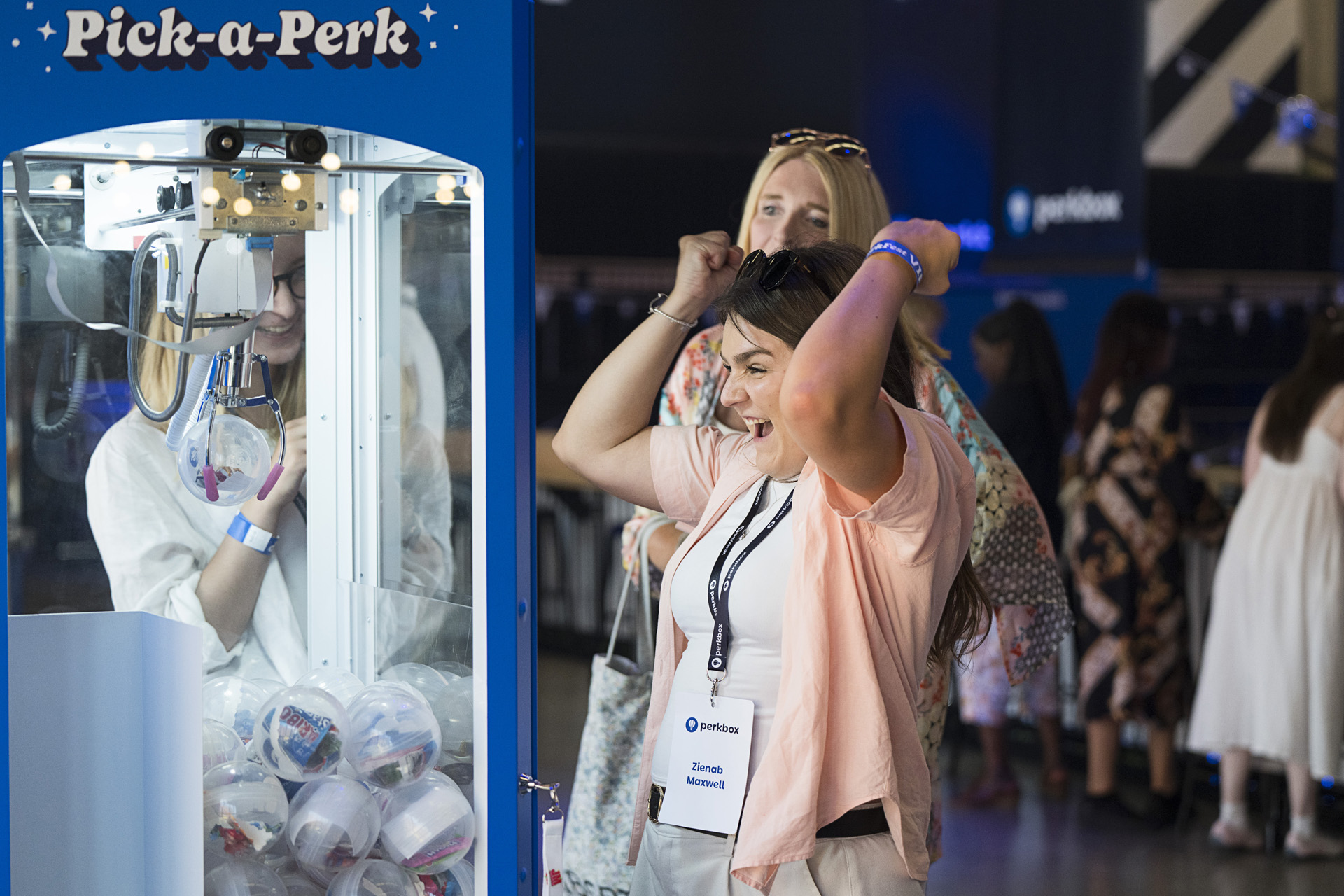 Two colleagues cheering at a branded claw grabber machine on the event floor