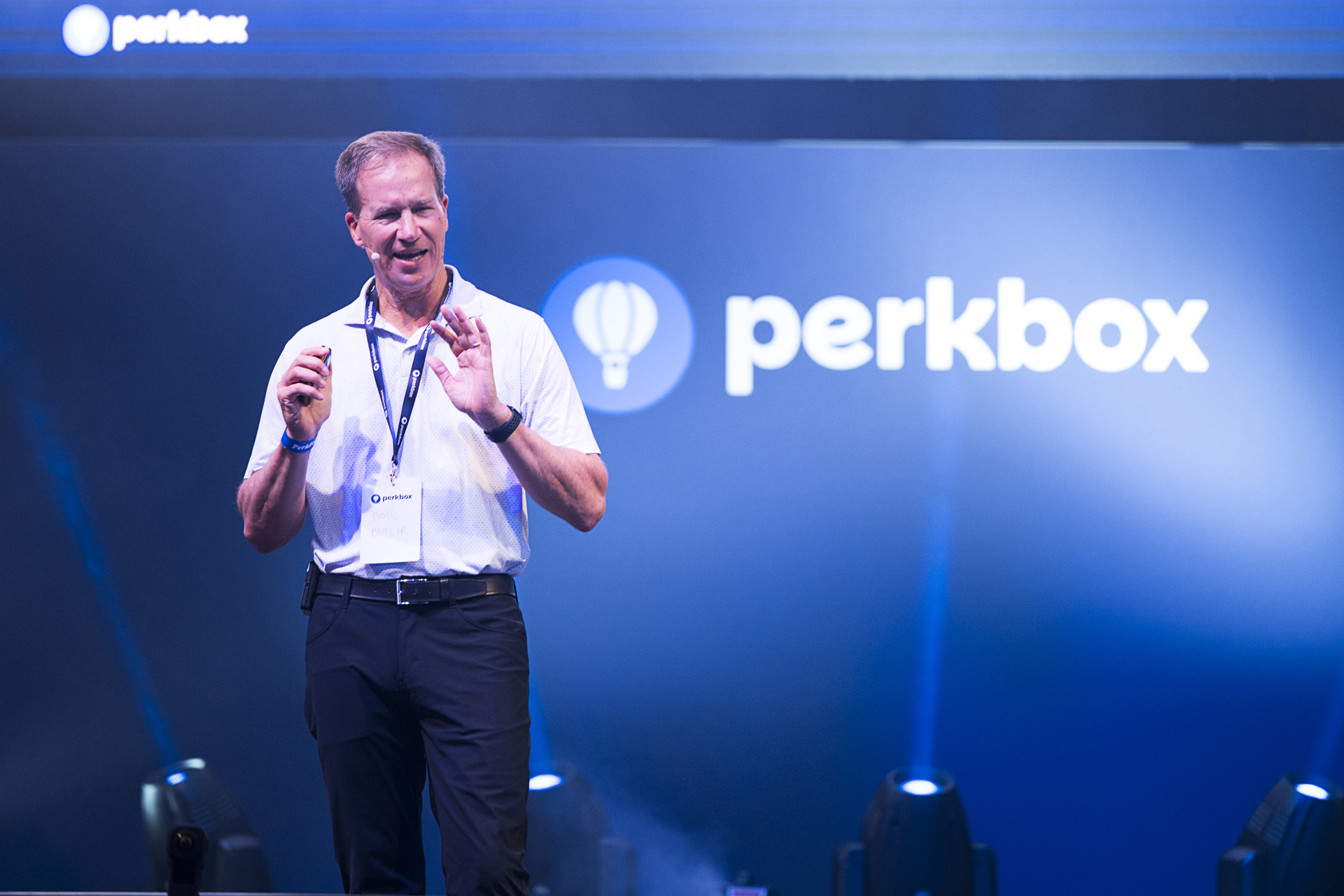 A speaker in a white shirt presenting on stage in front of a large company logo