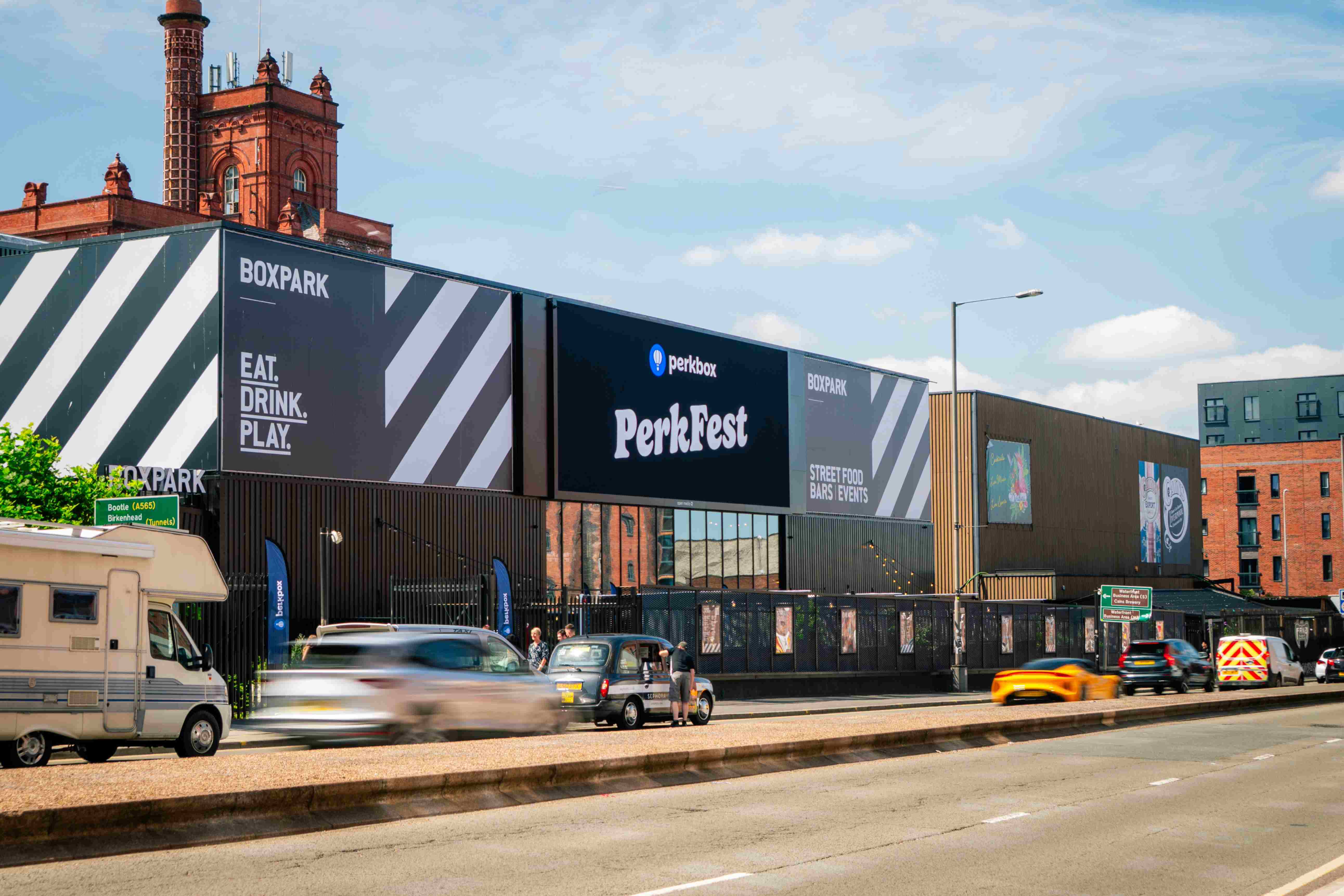 A large event billboard on the side of a Boxpark venue beside a road