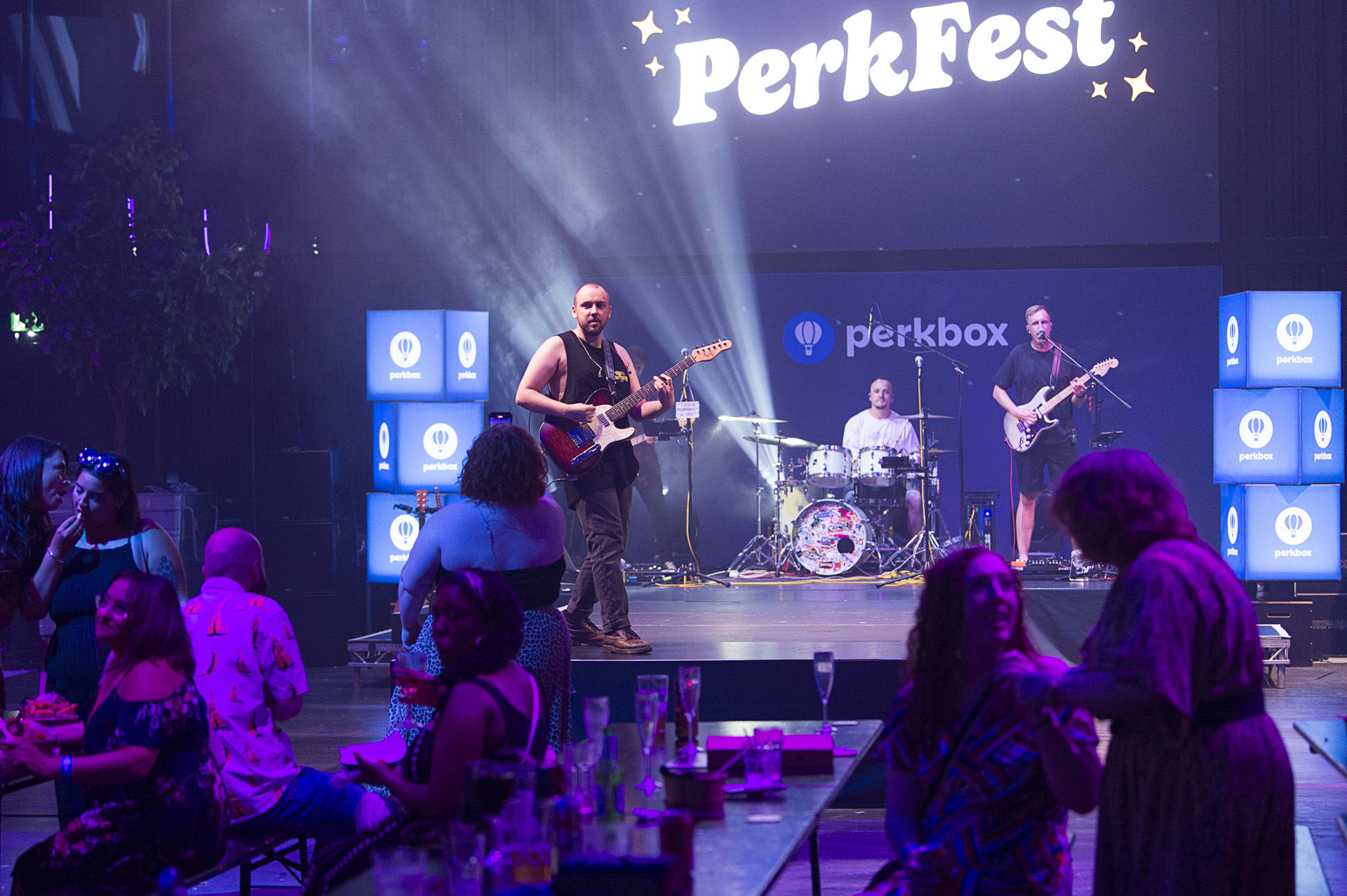 A live band playing on a lit stage while guests watch from long tables
