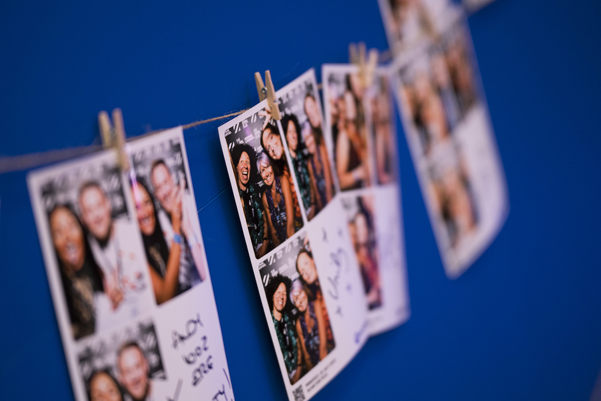 Printed photo booth strips pegged to a line against a blue backdrop