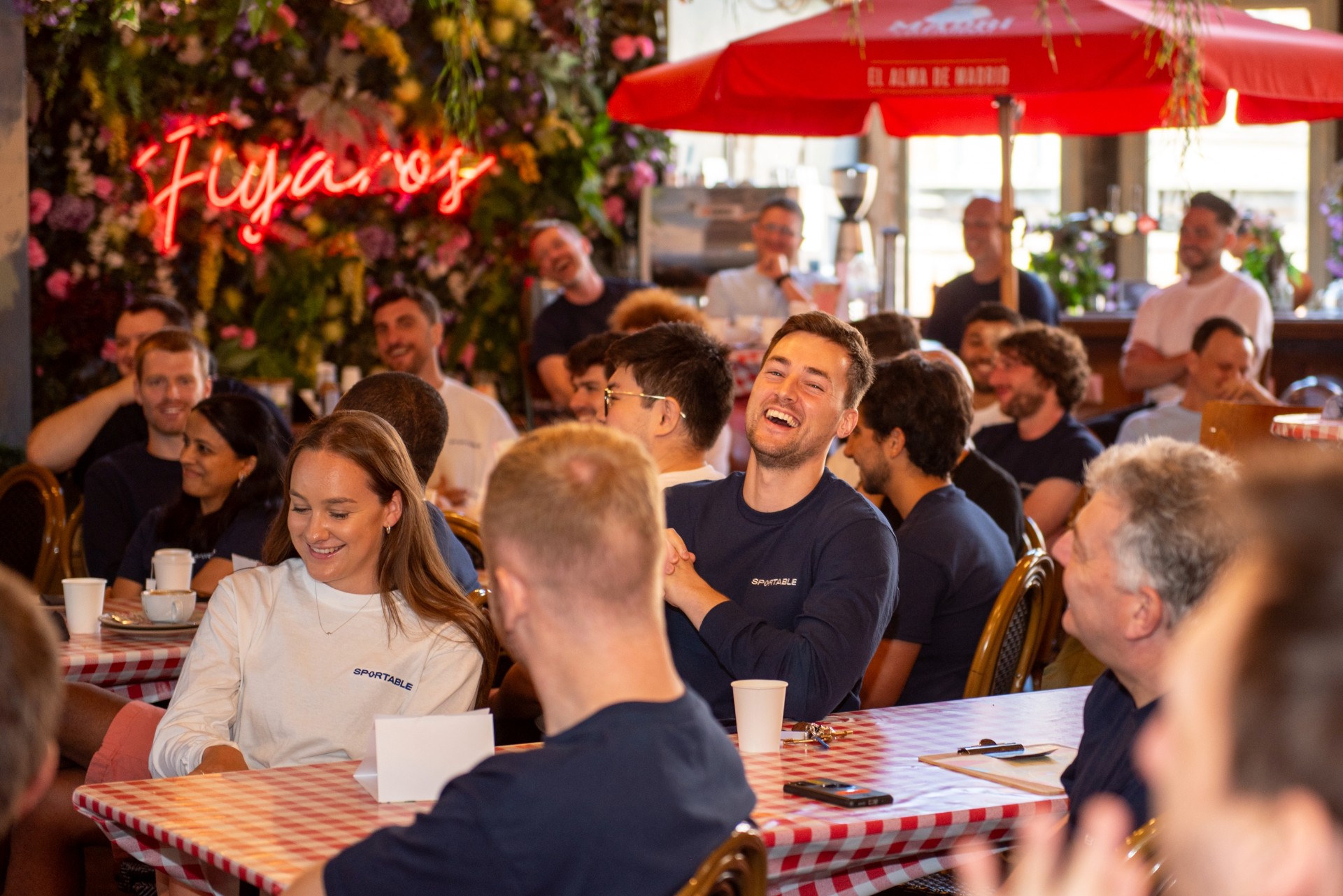 Colleagues in matching team shirts laughing around checked tables in a bright restaurant