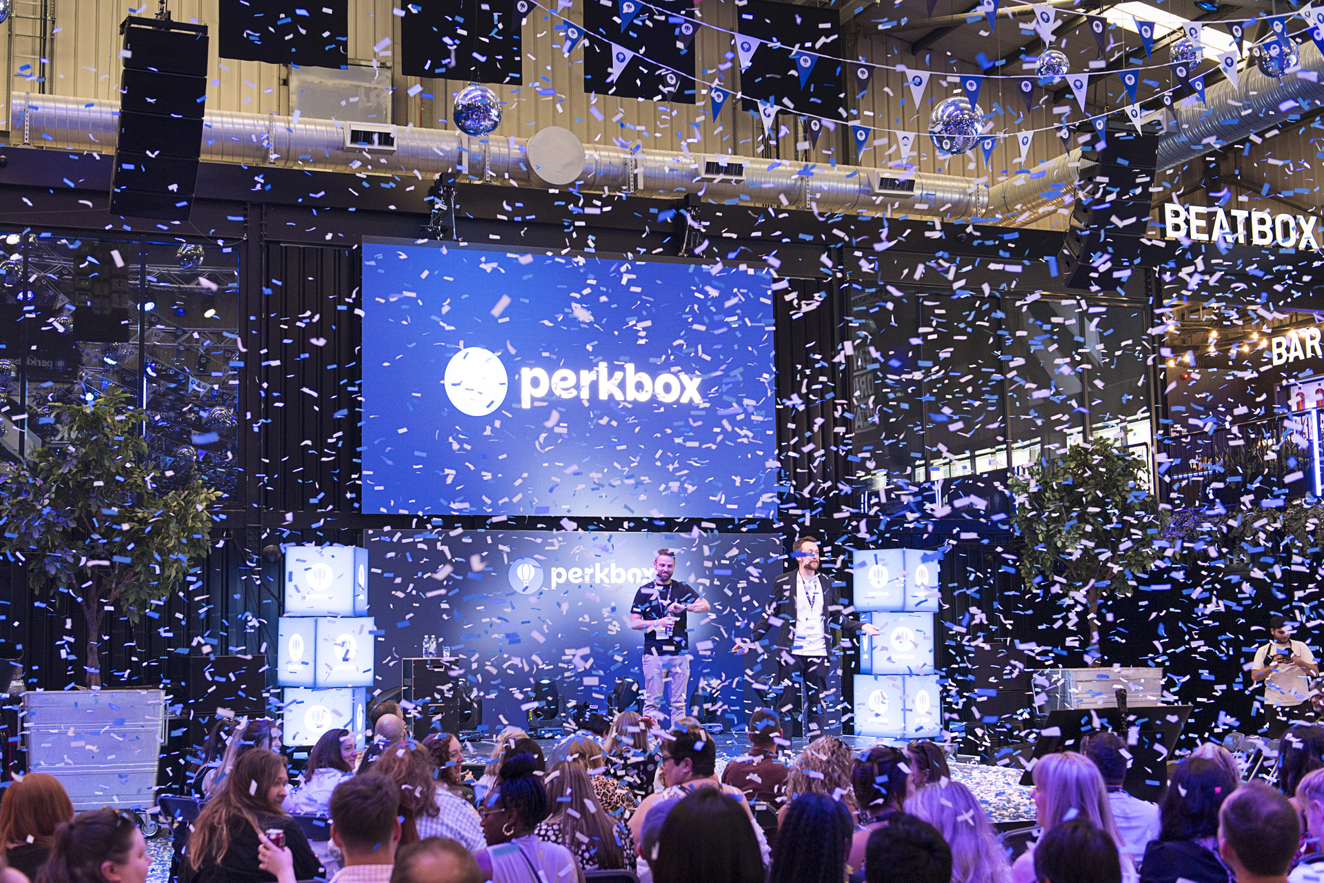 Confetti falling over an audience watching a speaker on a brightly lit stage