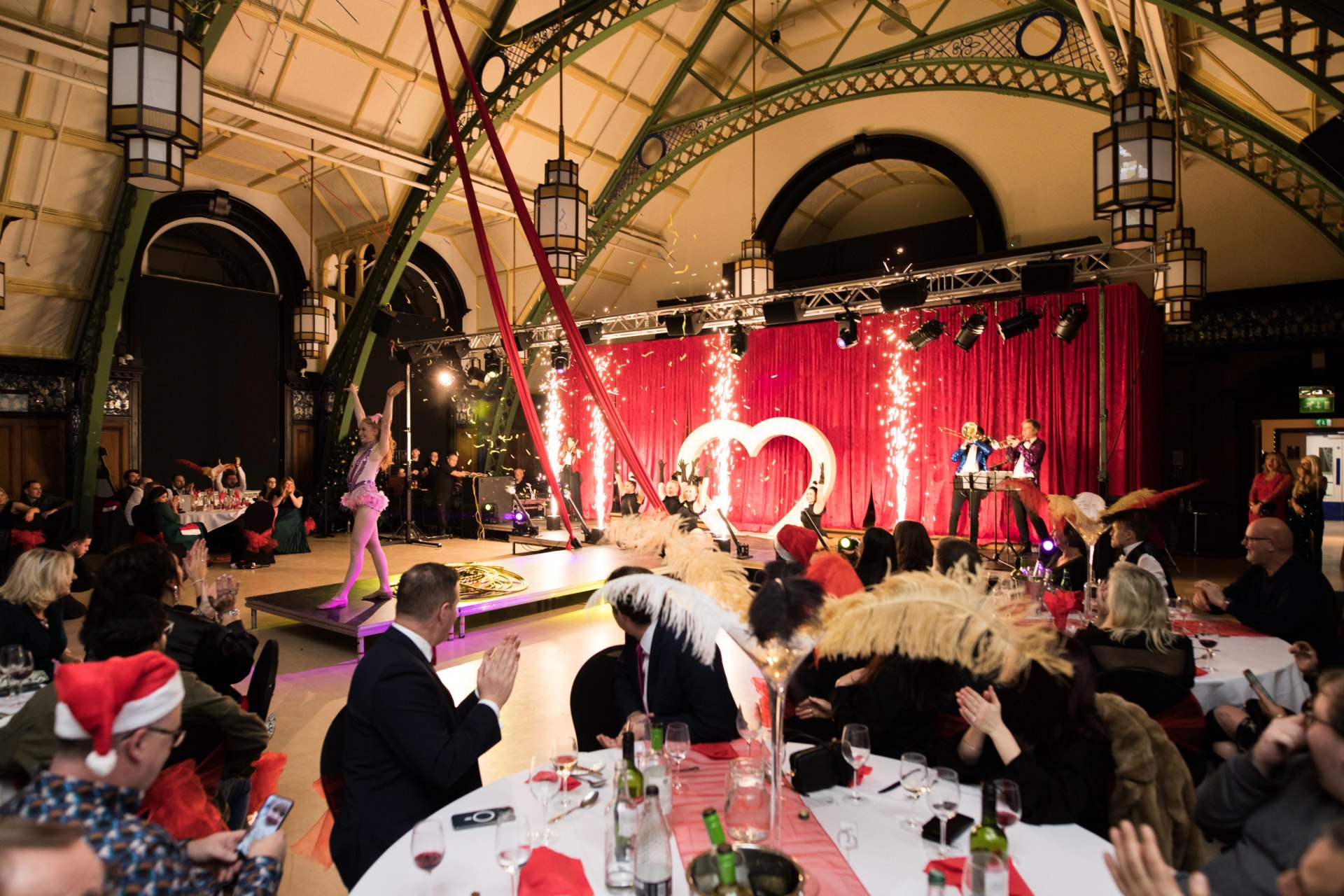 Aerial performers and a heart-shaped light display on stage above seated party diners