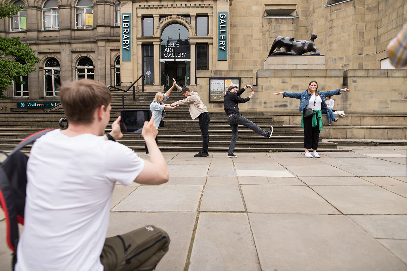 A man photographing colleagues leaping in the air outside a city art gallery