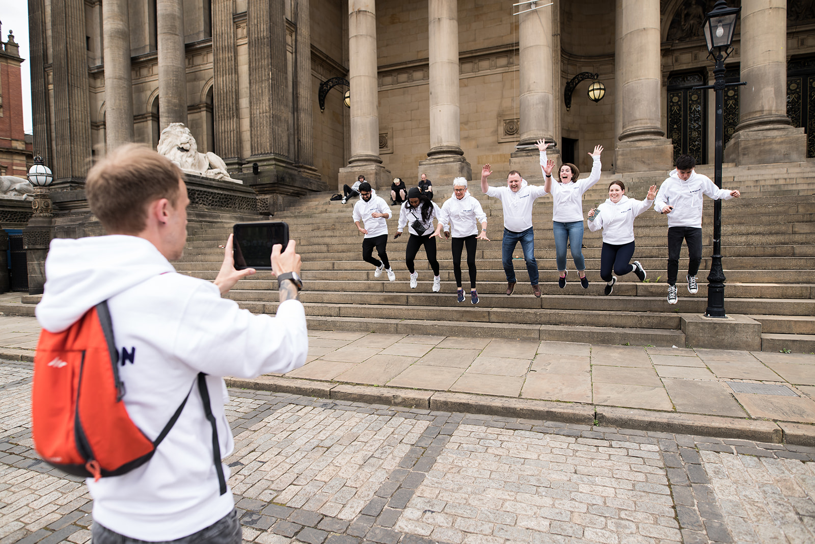 A colleague photographing teammates jumping on the steps of a civic building