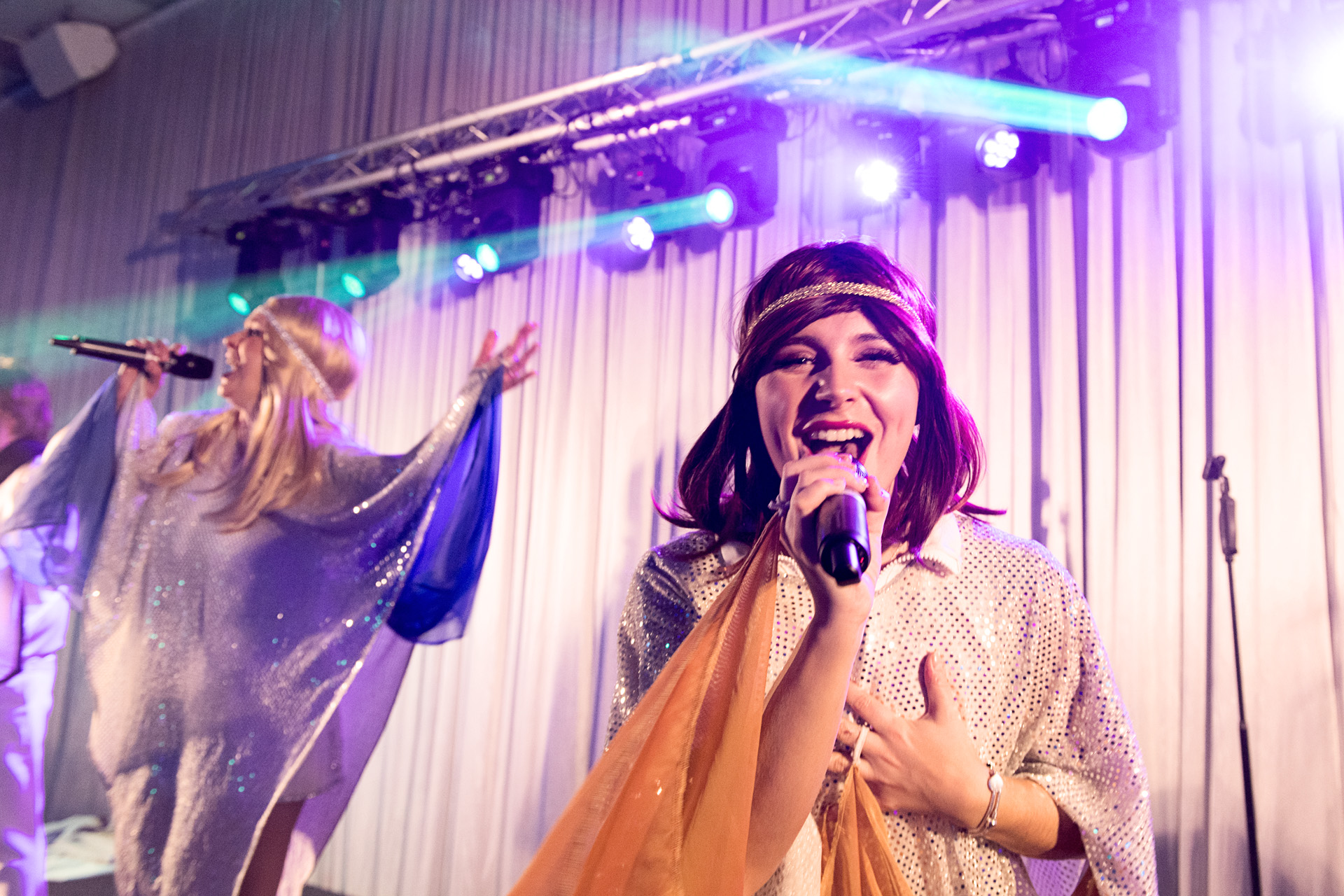 Two vocalists performing in flowing costumes under purple stage lighting