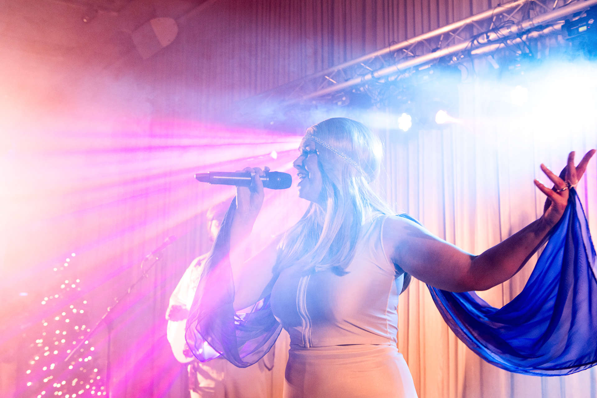 A singer performing with a flowing blue scarf under pink and purple stage lights