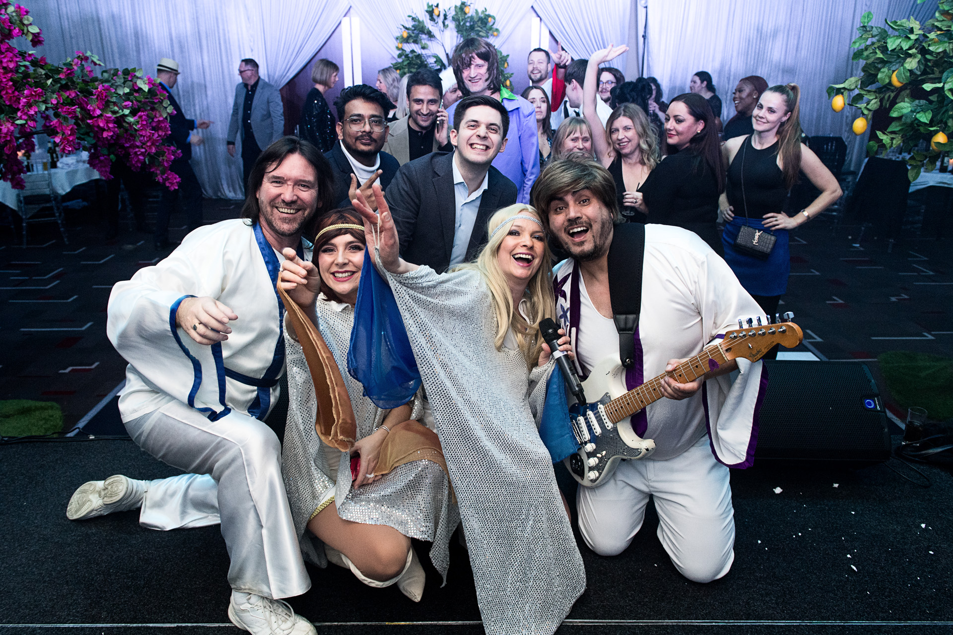 Guests crouching for a group photo with performers in white costumes after the show