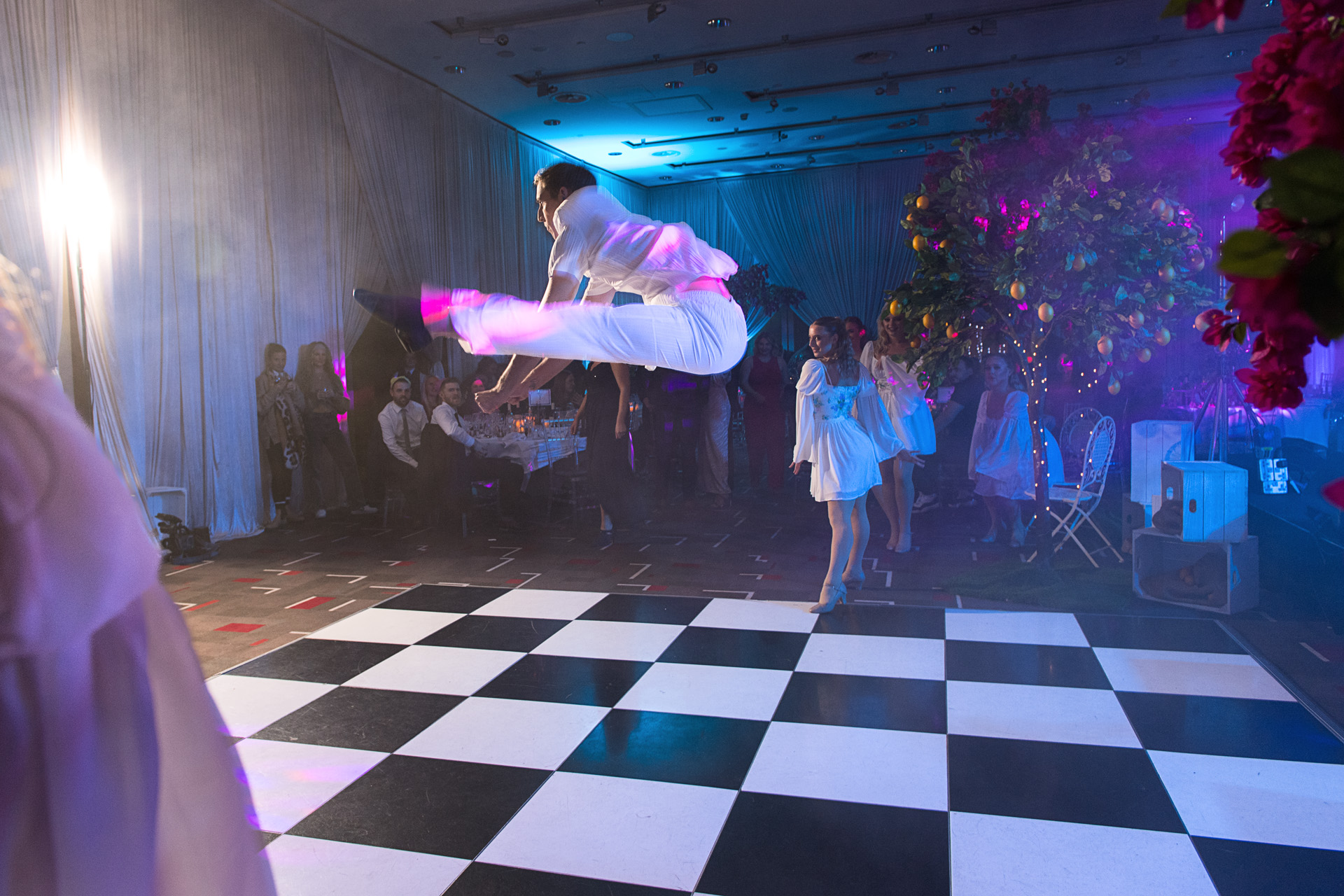 A dancer leaping across a black and white chequered dance floor at a themed party