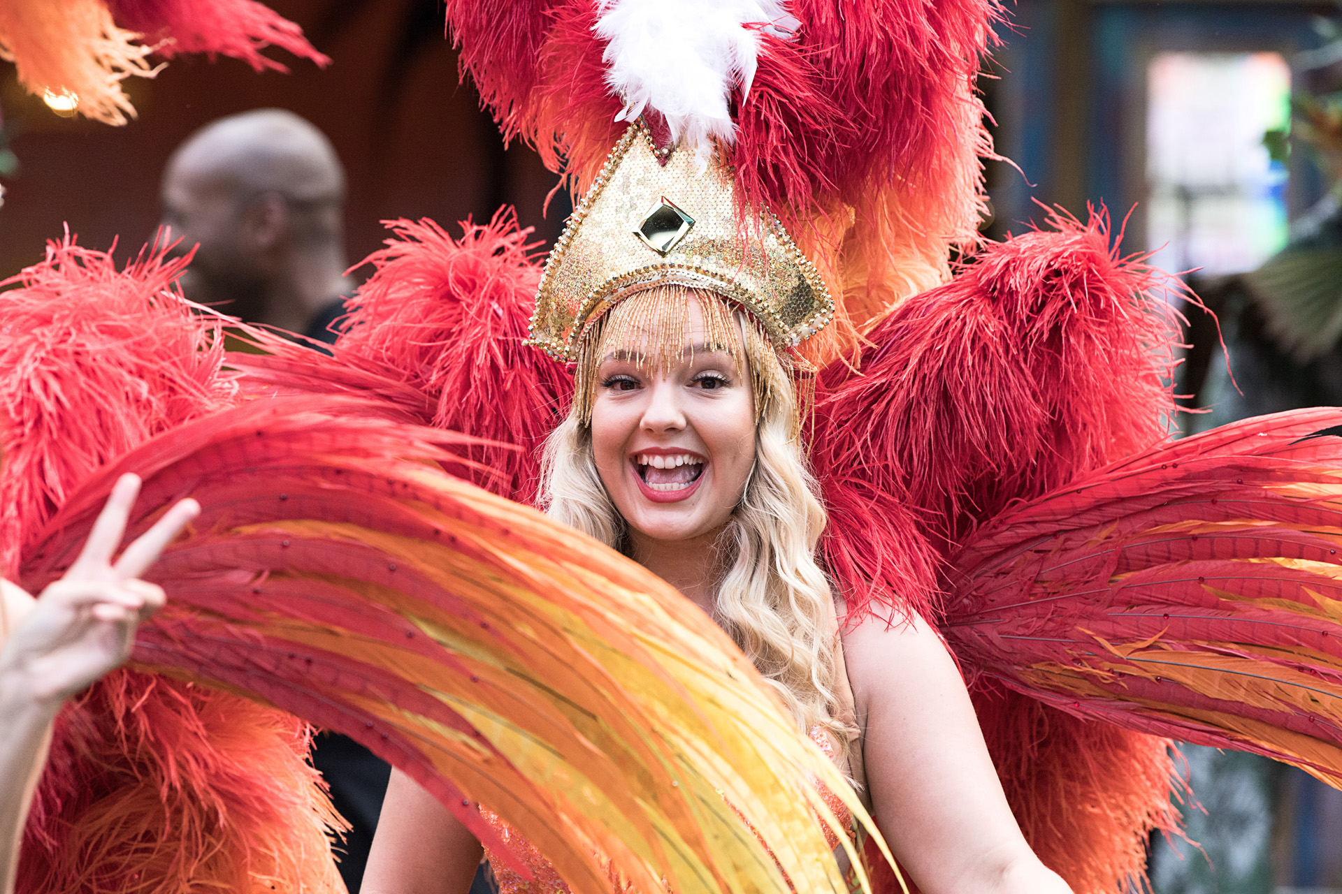 A carnival dancer in a red and gold feathered costume smiling at the camera
