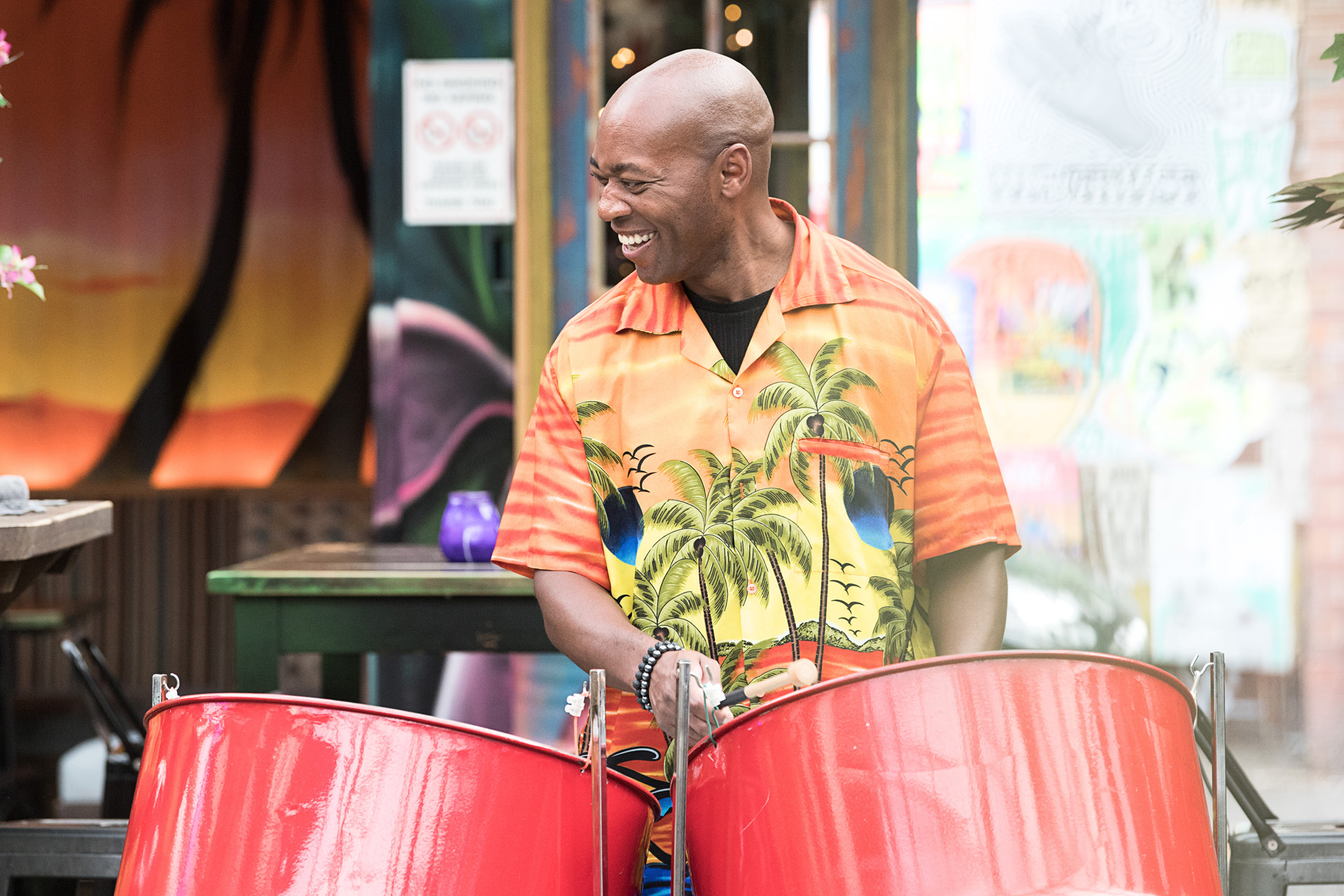 A steel pan drummer smiling as he plays a set of red drums