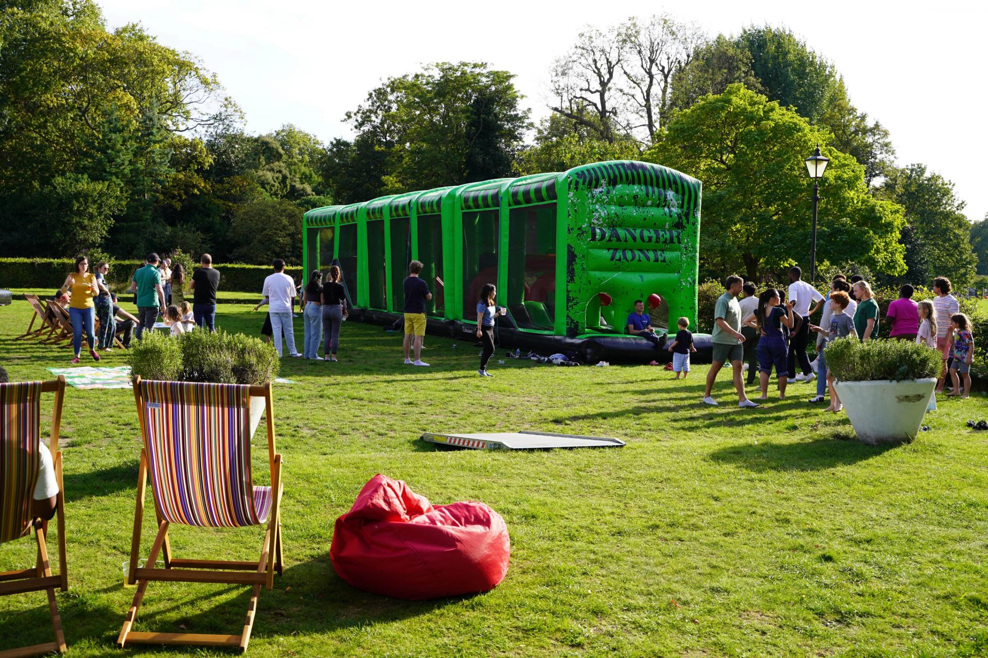 An inflatable assault course and deck chairs set out on a park lawn for families