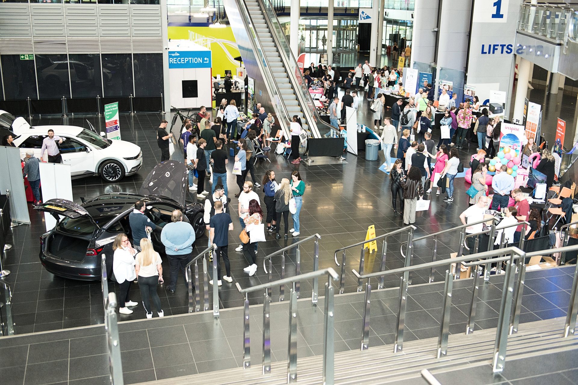 Employees browsing benefits stands around a car display in a busy office atrium