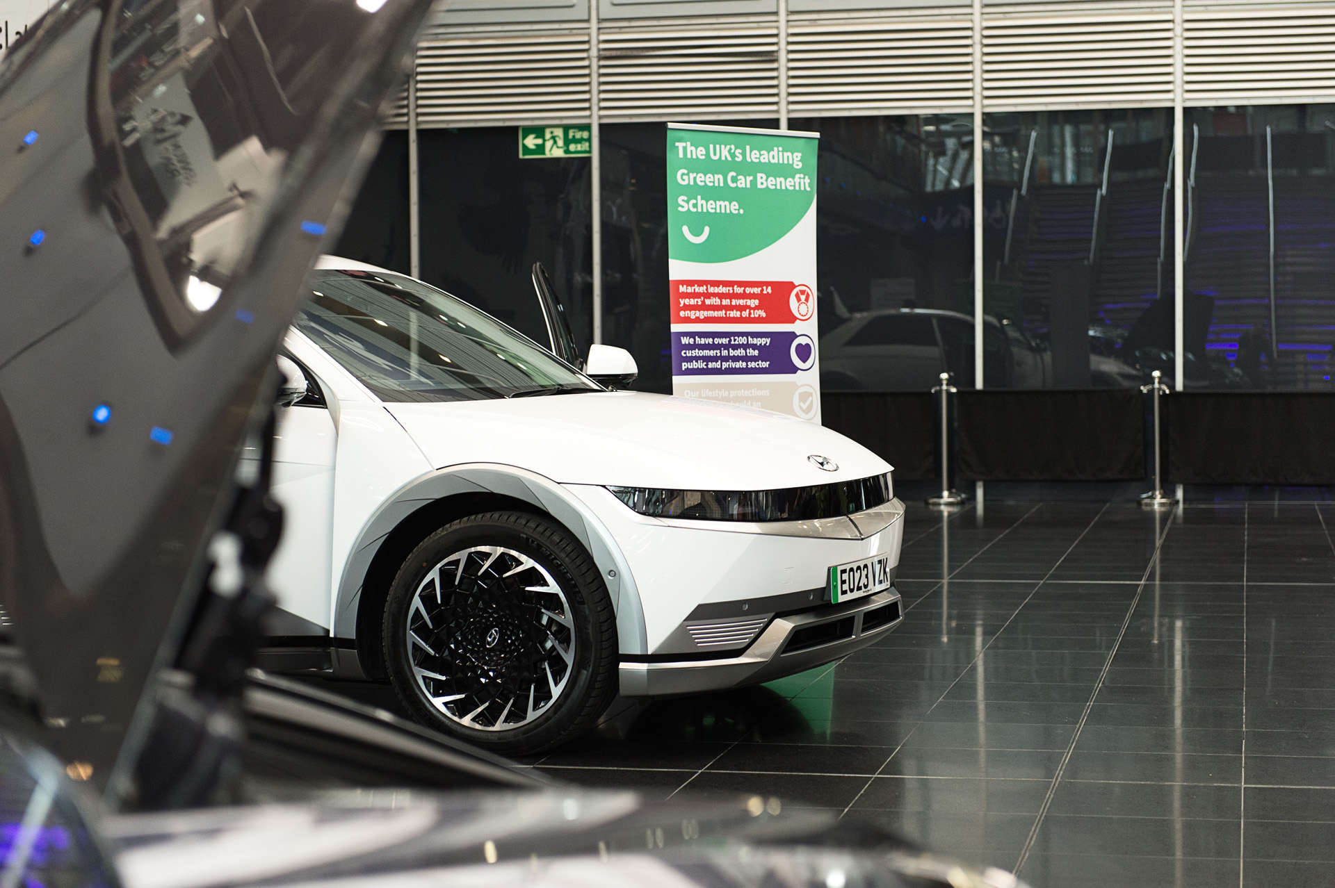 A white electric car on display next to a green car benefit scheme sign