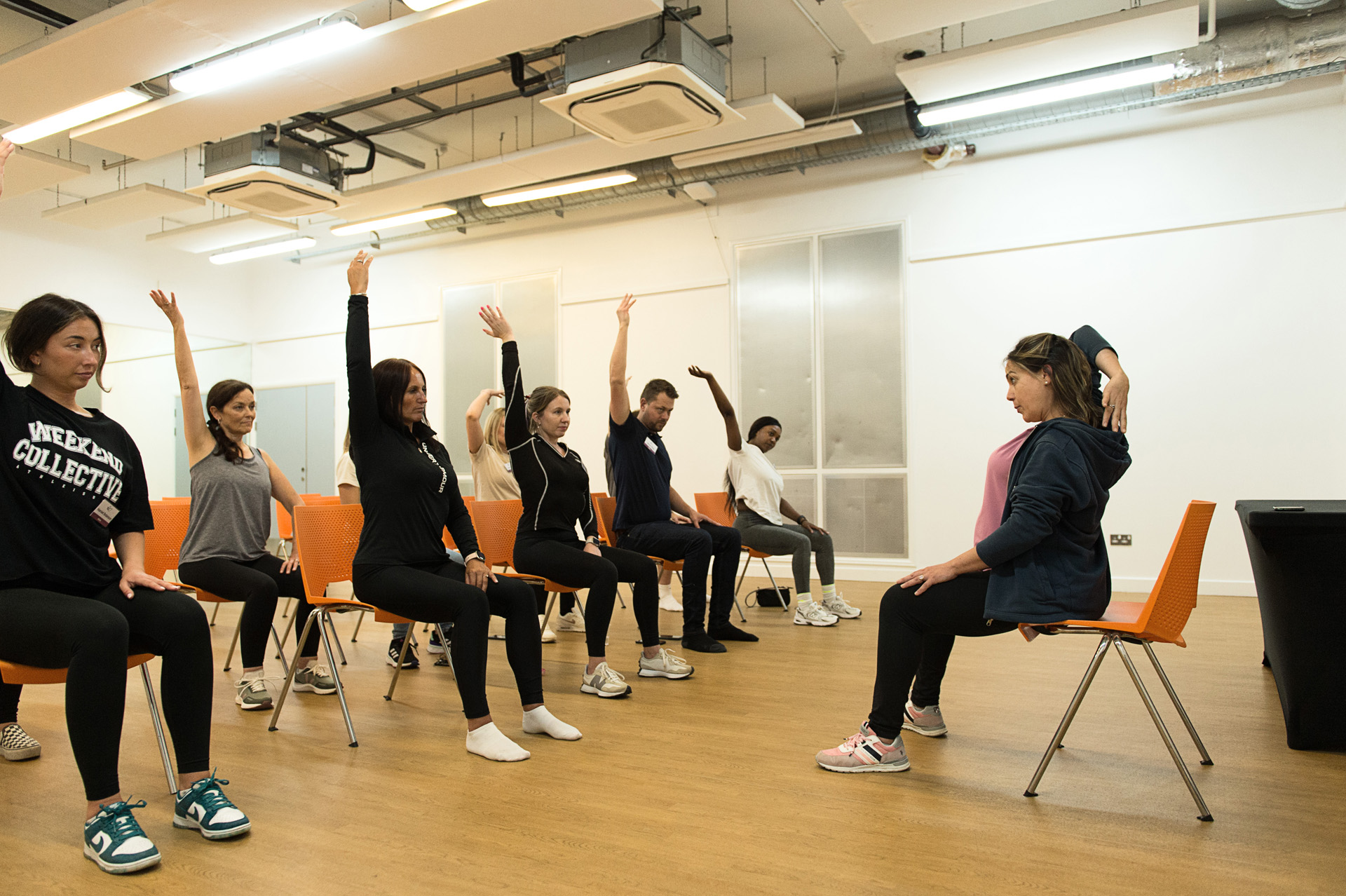 Employees following a seated stretching class led by an instructor in a bright room