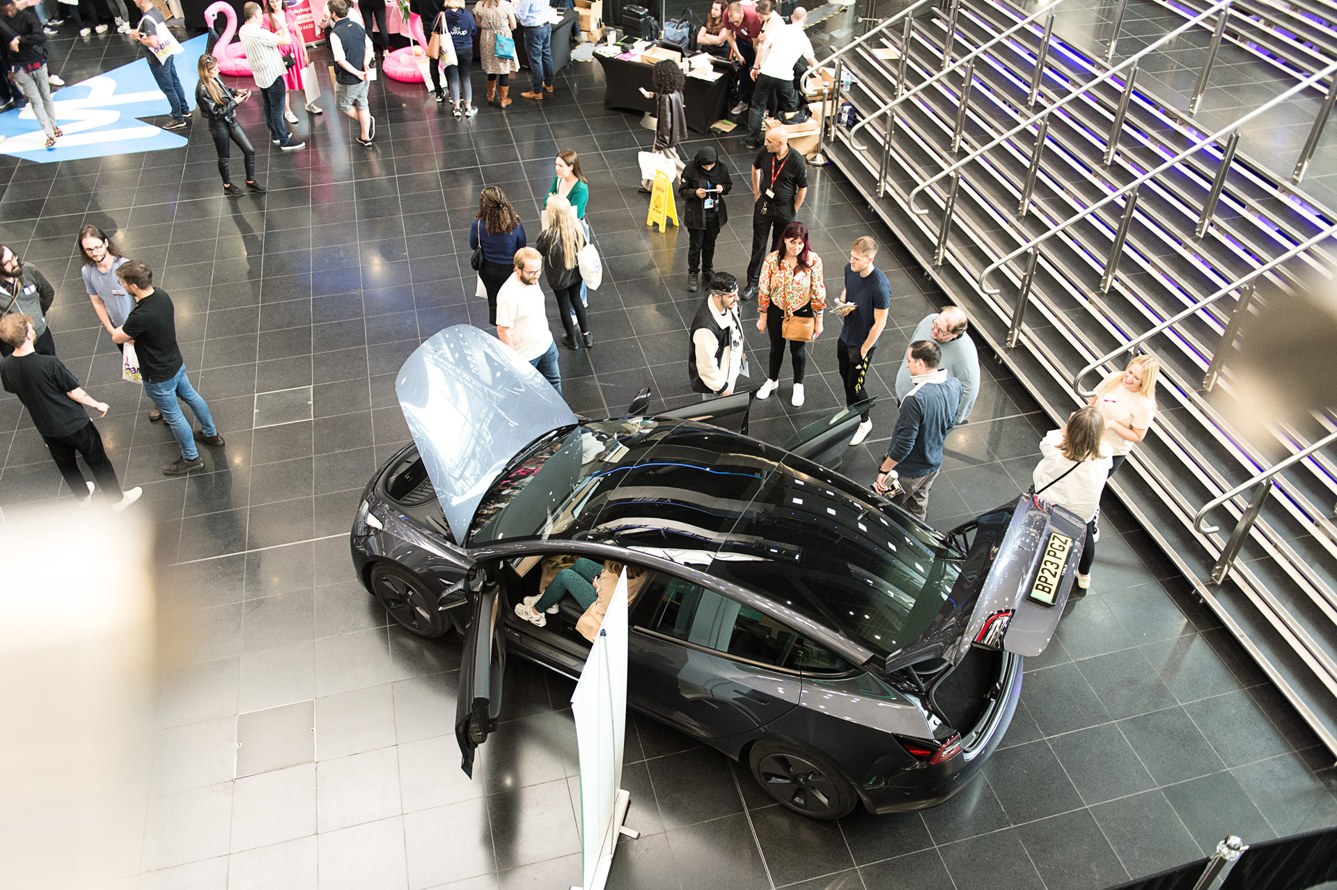 An overhead view of colleagues moving between exhibitor stands beside a display car