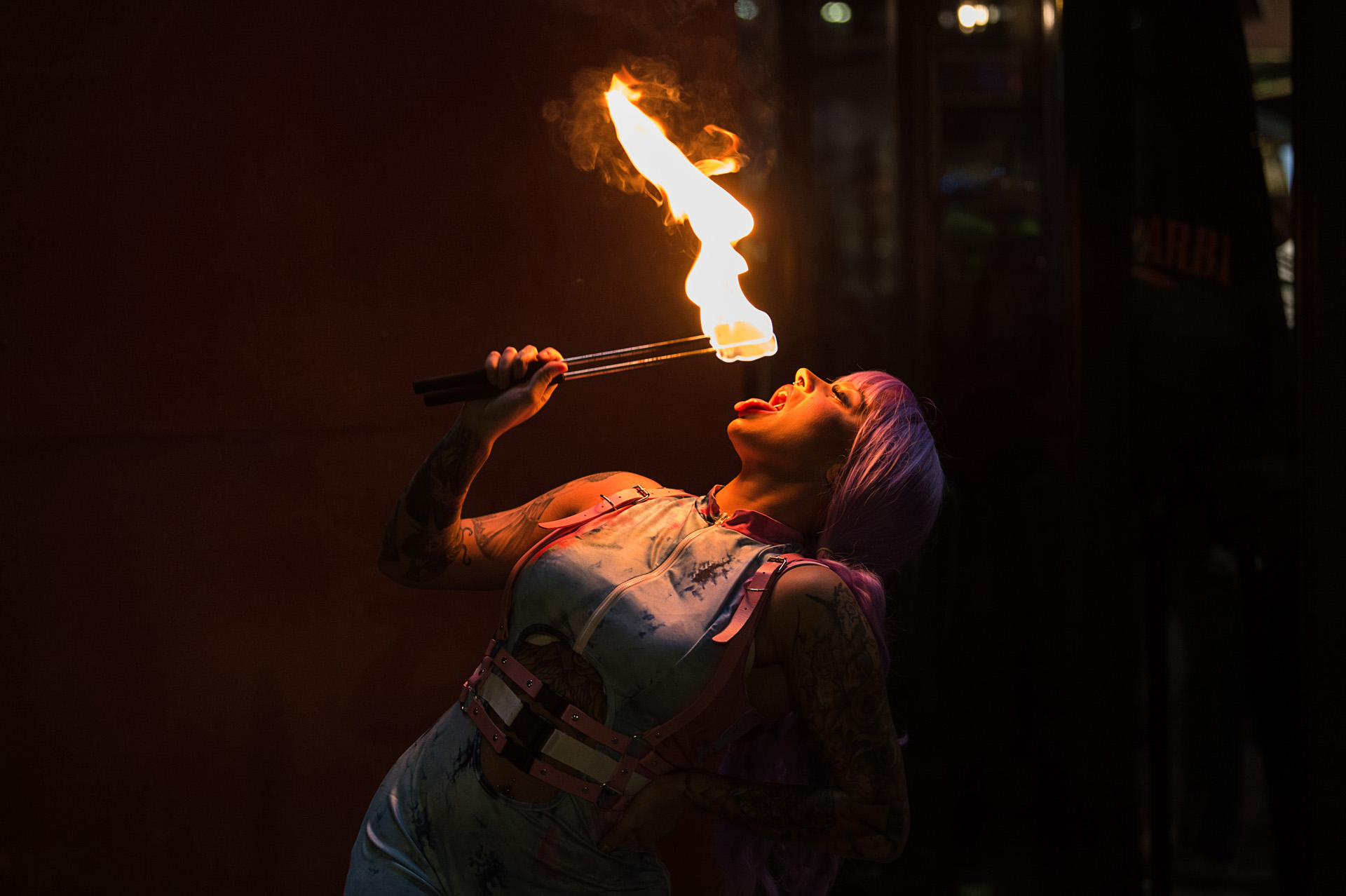 A fire performer breathing flame from a torch in a darkened venue