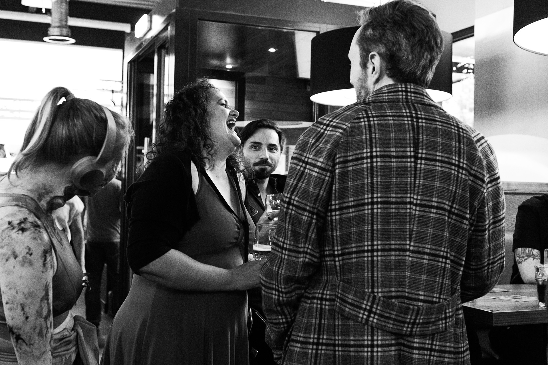 Guests laughing over drinks in a black and white photograph of the launch party