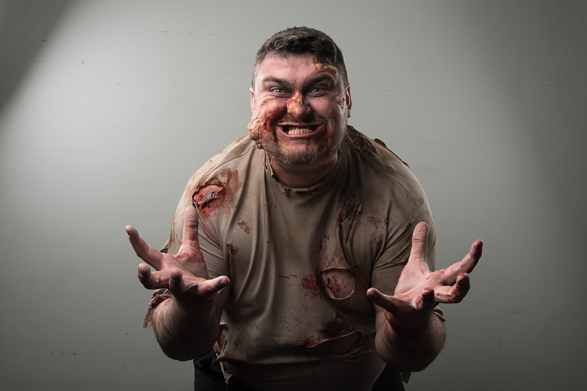 A performer in bloodied zombie makeup snarling towards the camera in a studio shot