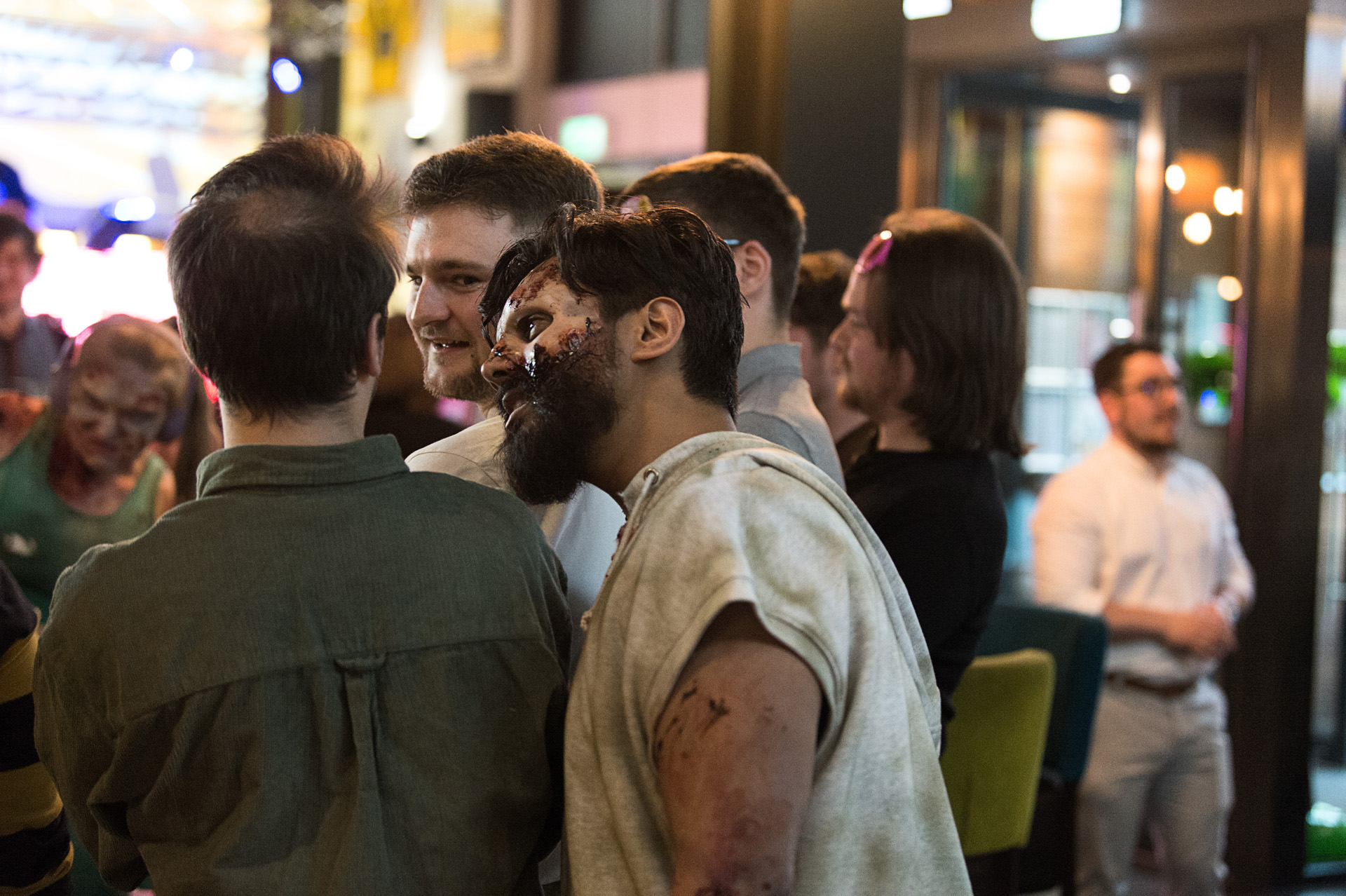 A costumed zombie performer mingling with guests standing with drinks at the launch