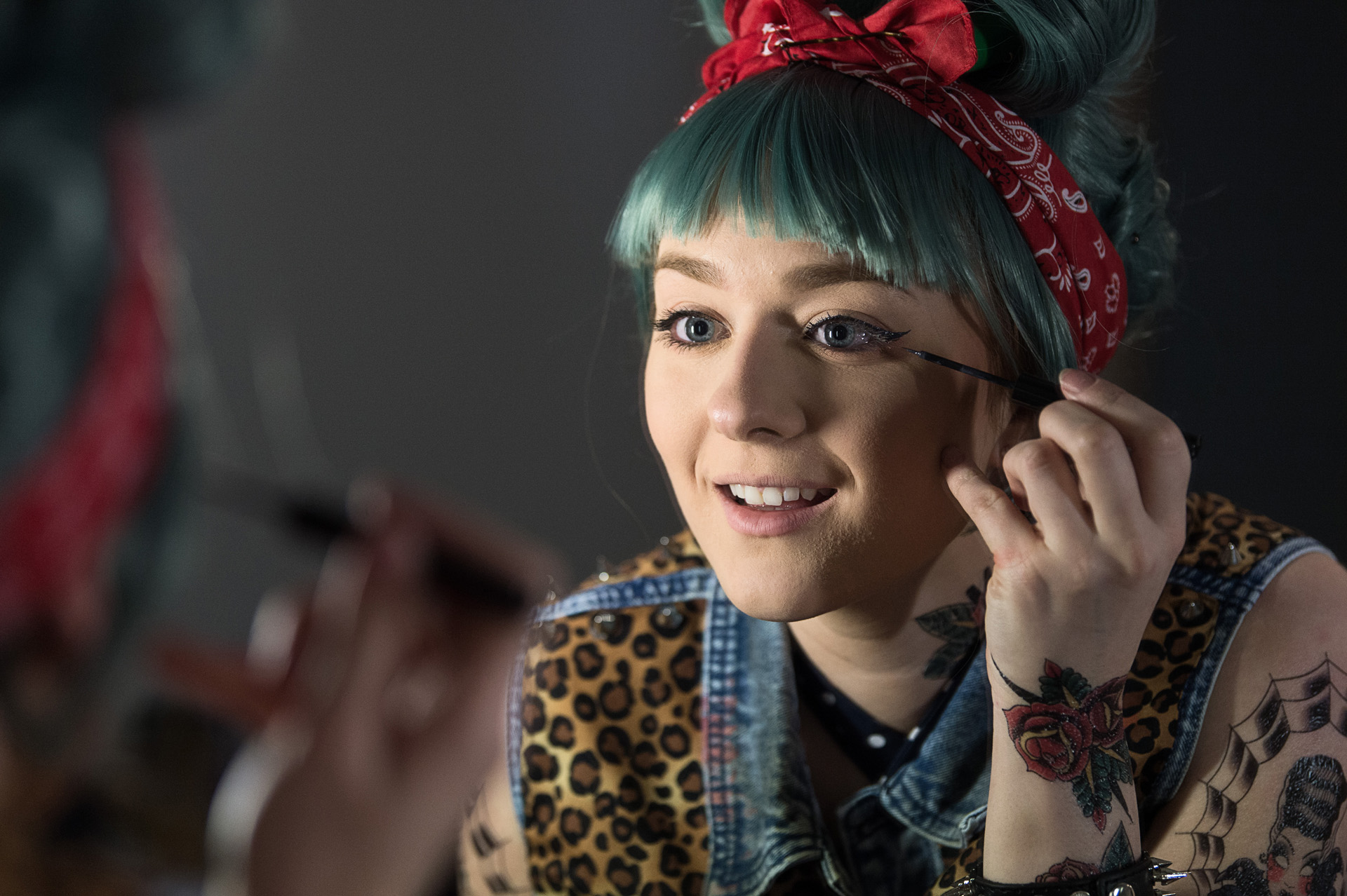 A prosthetics artist with teal hair getting ready in front of a mirror