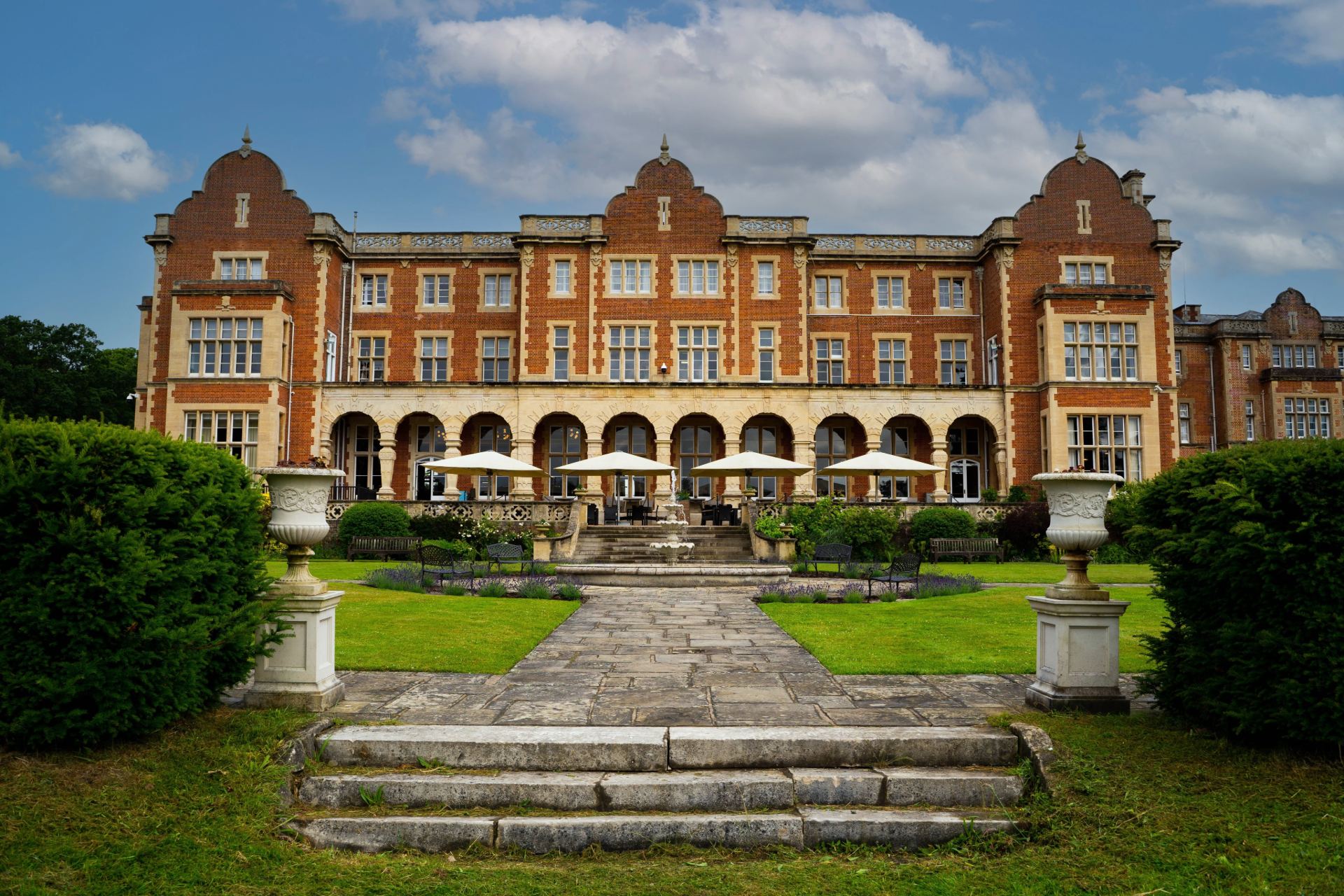 A red brick country house hotel with formal lawns and terrace parasols