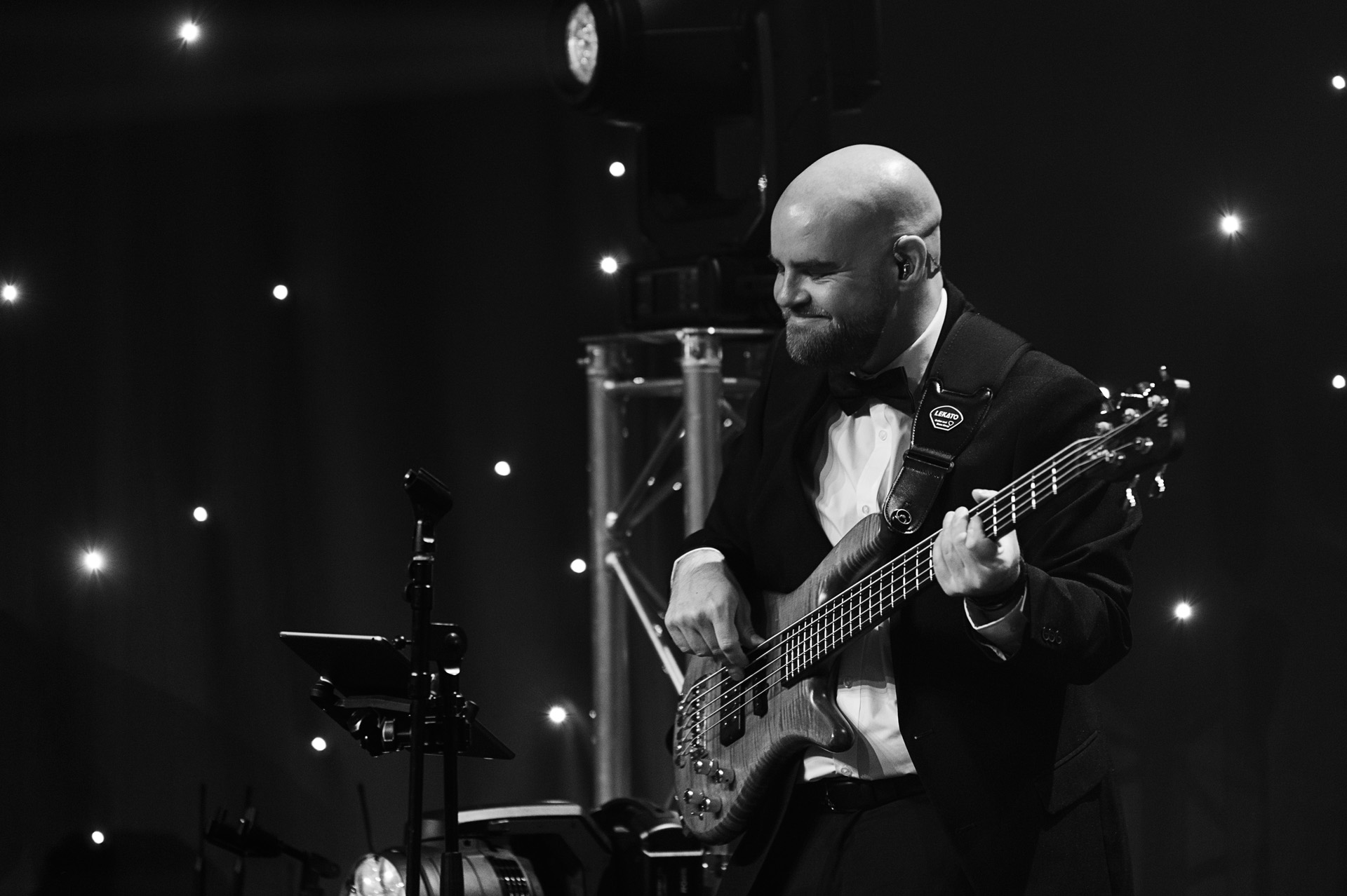 A bass guitarist in black tie performing in front of a starcloth backdrop