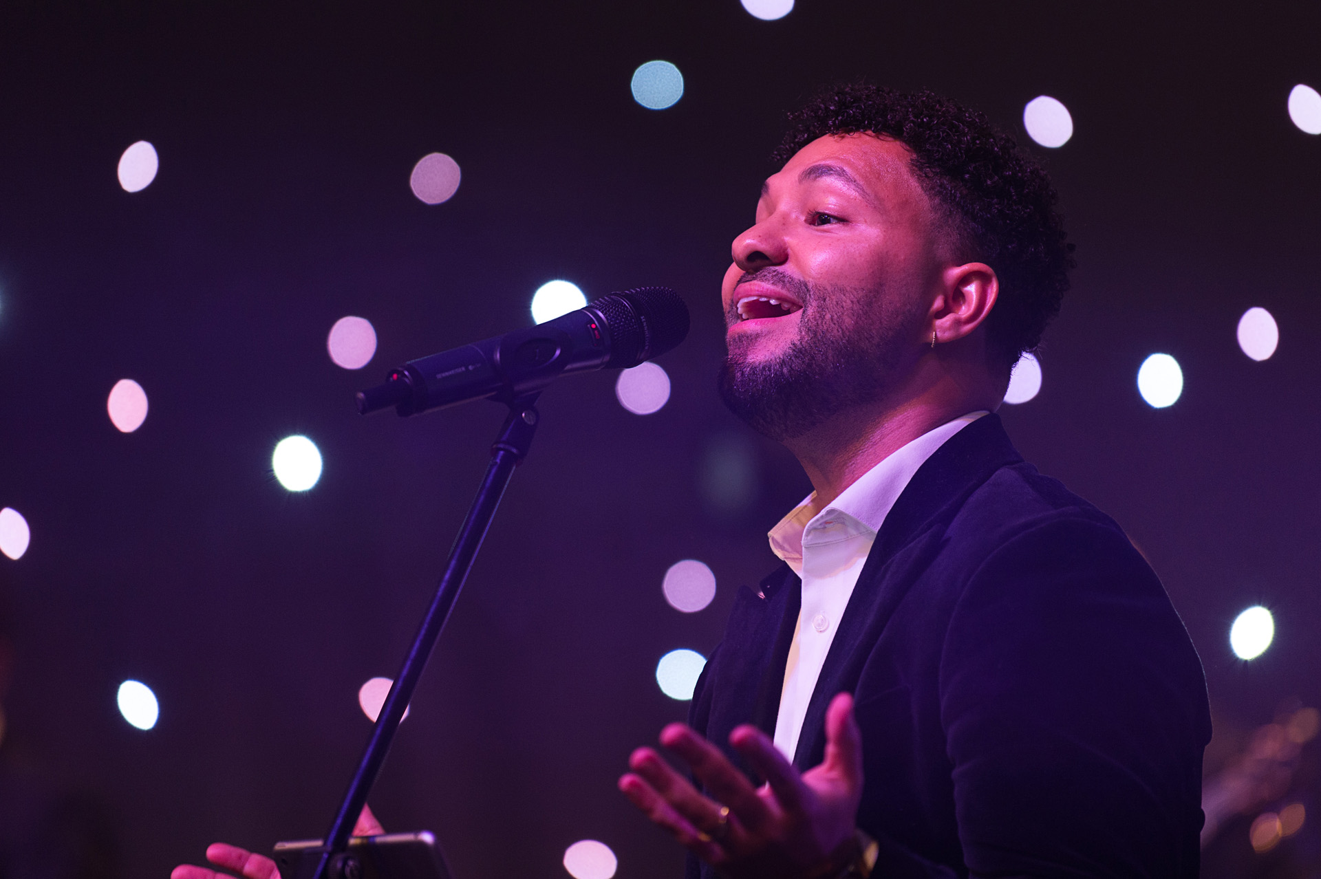 A vocalist in a dark suit singing under purple lighting at a winter party