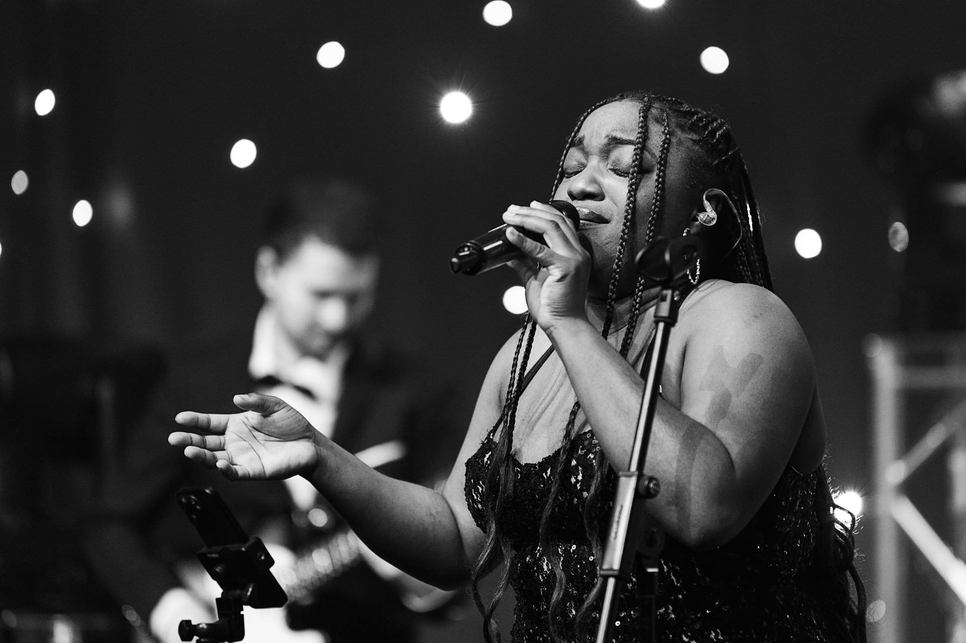 A vocalist performing with the band behind her in a black and white shot