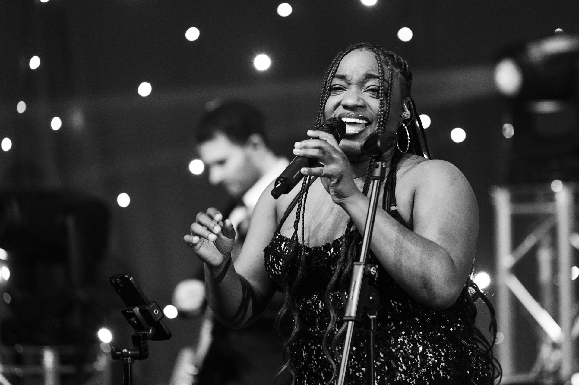 A singer smiling mid-song in front of a starlit backdrop in black and white