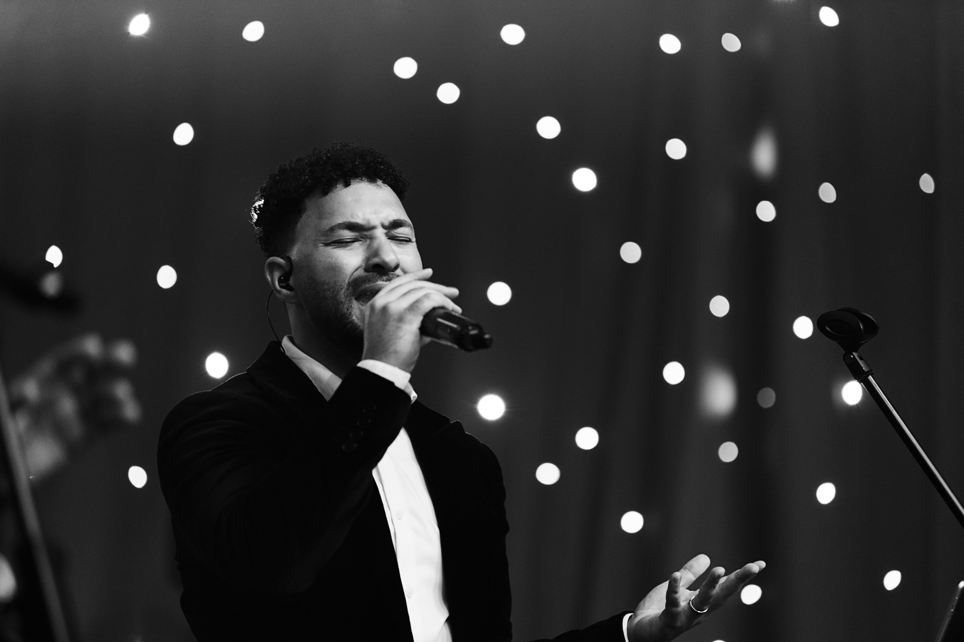 A male vocalist singing into a microphone against a starcloth in black and white