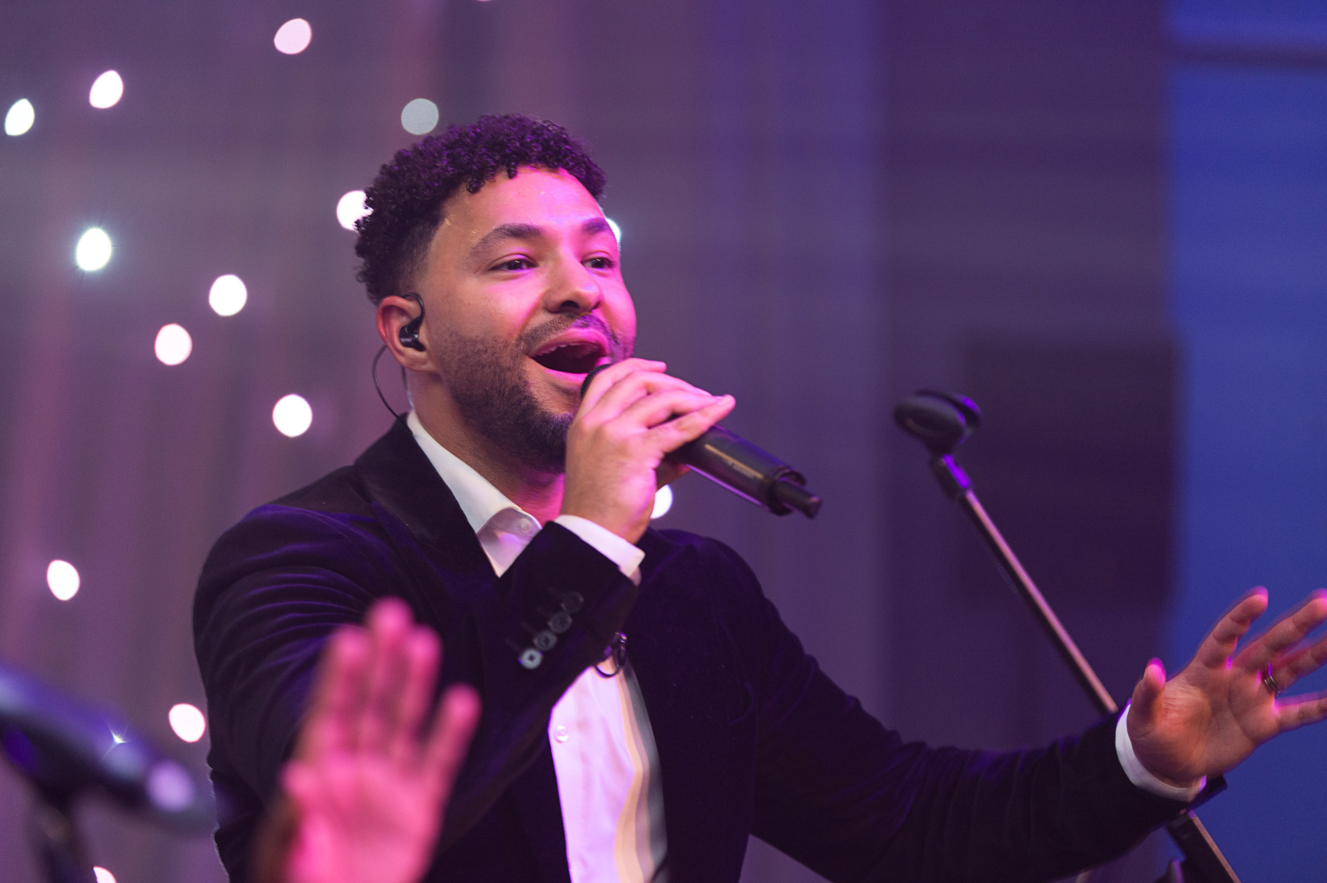 A vocalist singing with hands raised in the foreground at a winter party