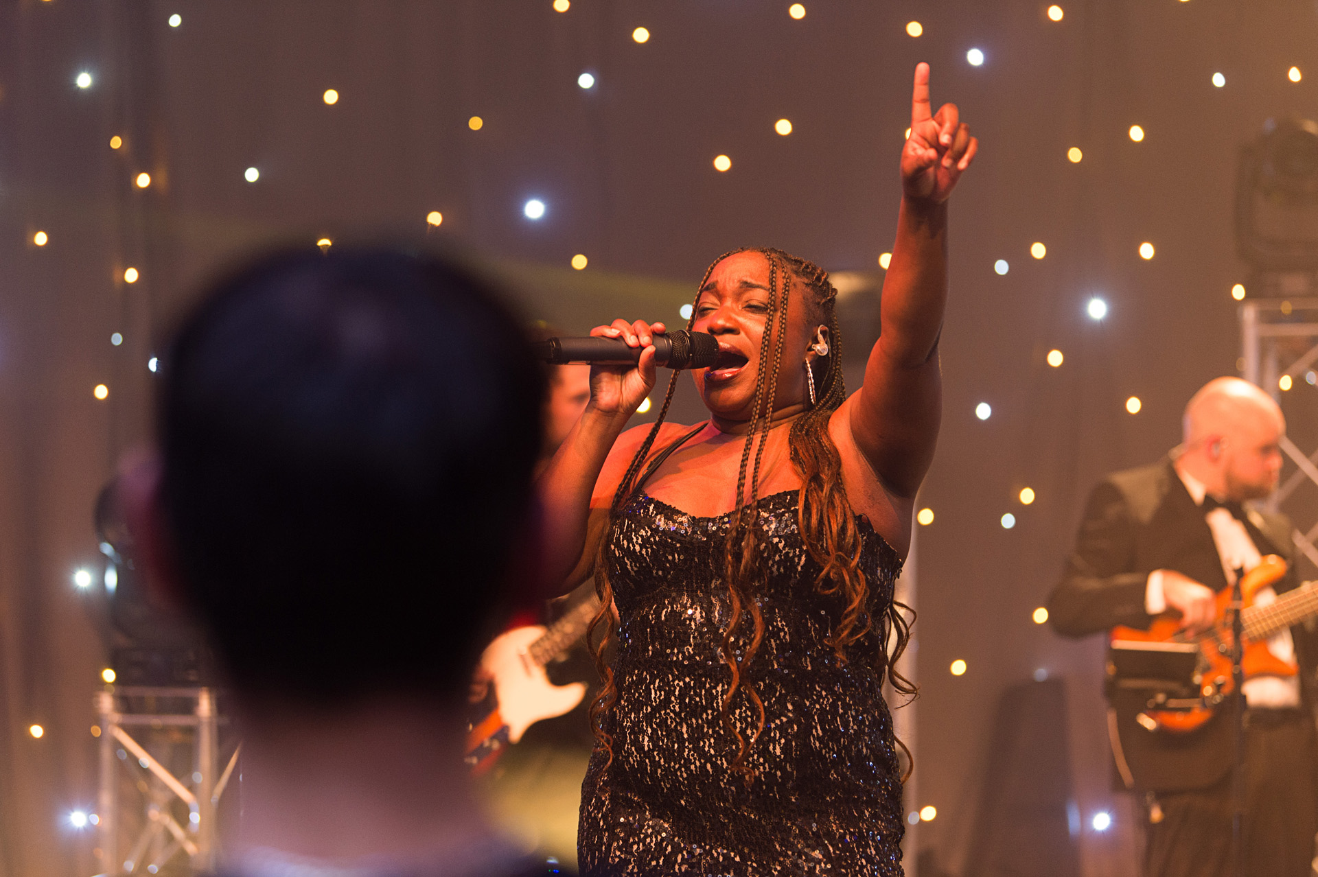 A singer pointing upwards mid-performance as the band plays behind her
