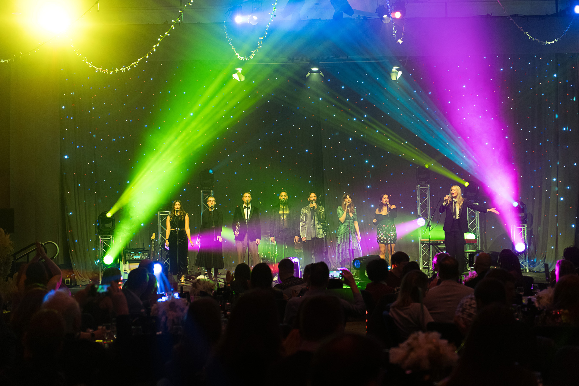 Performers on stage lit by green and pink beams above a seated audience