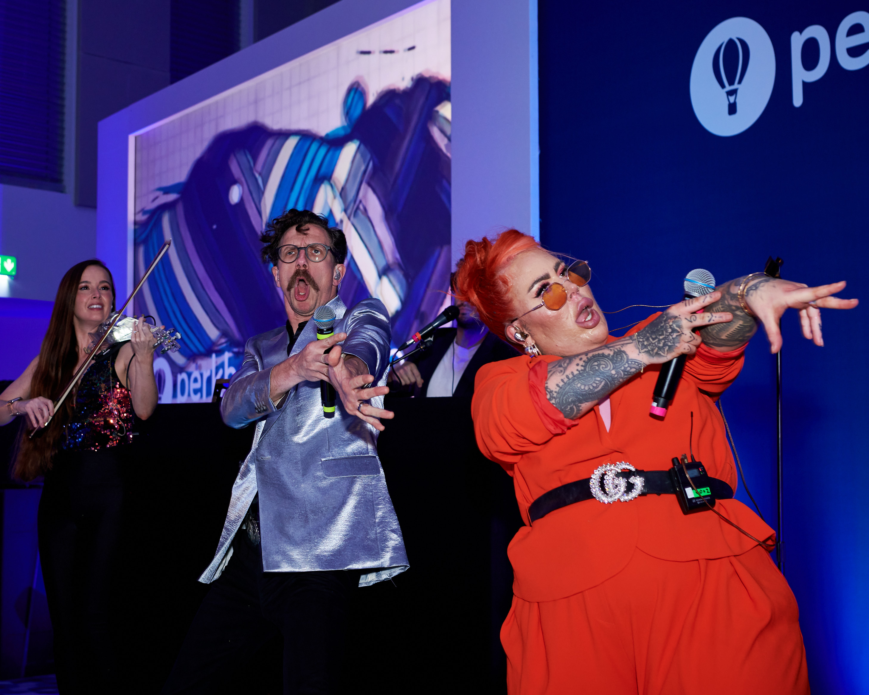 Performers in bold costumes singing together on stage in front of a screen