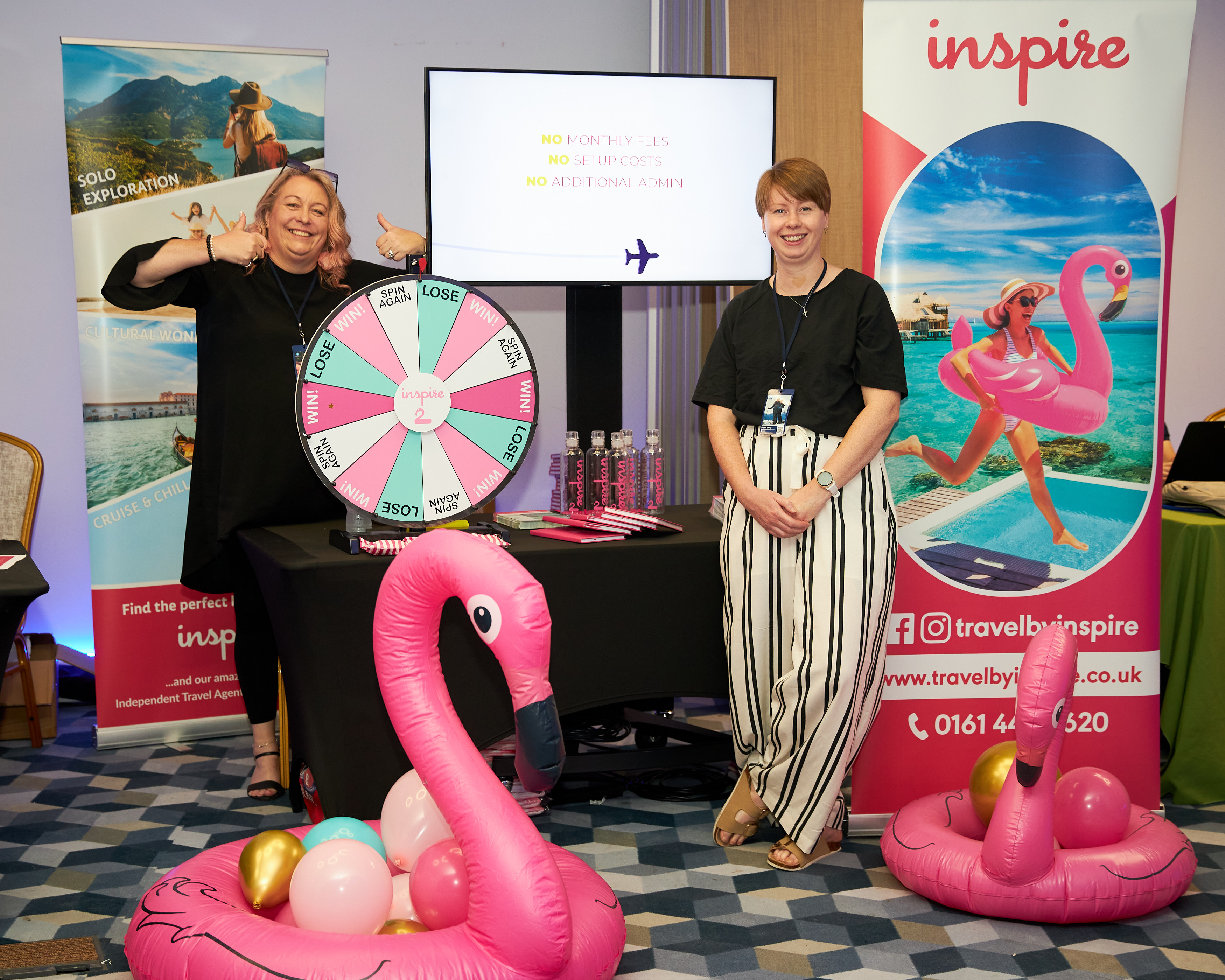 Two exhibitors beside a prize wheel and inflatable flamingos on a travel benefits stand