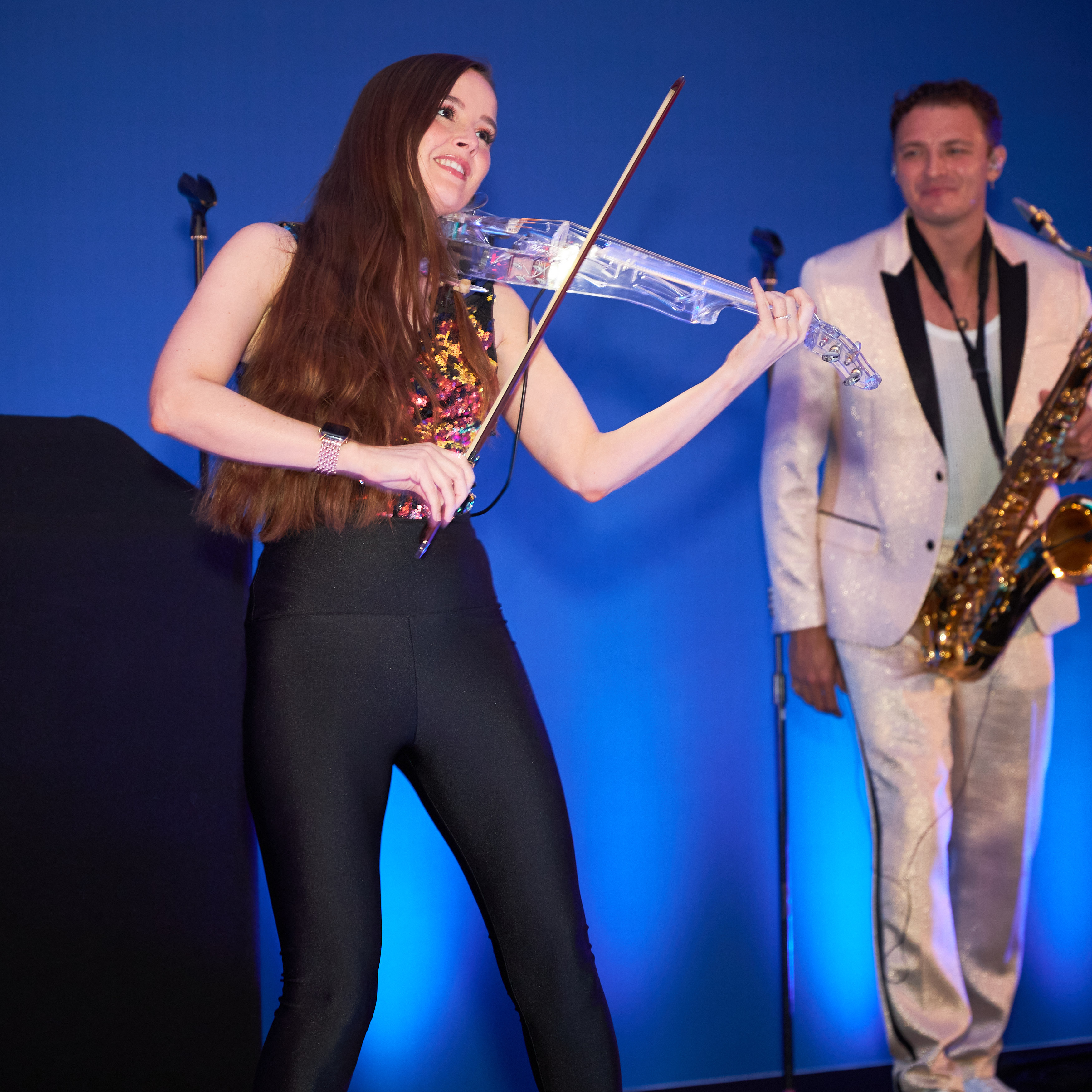 A violinist and saxophonist performing together against a blue lit backdrop