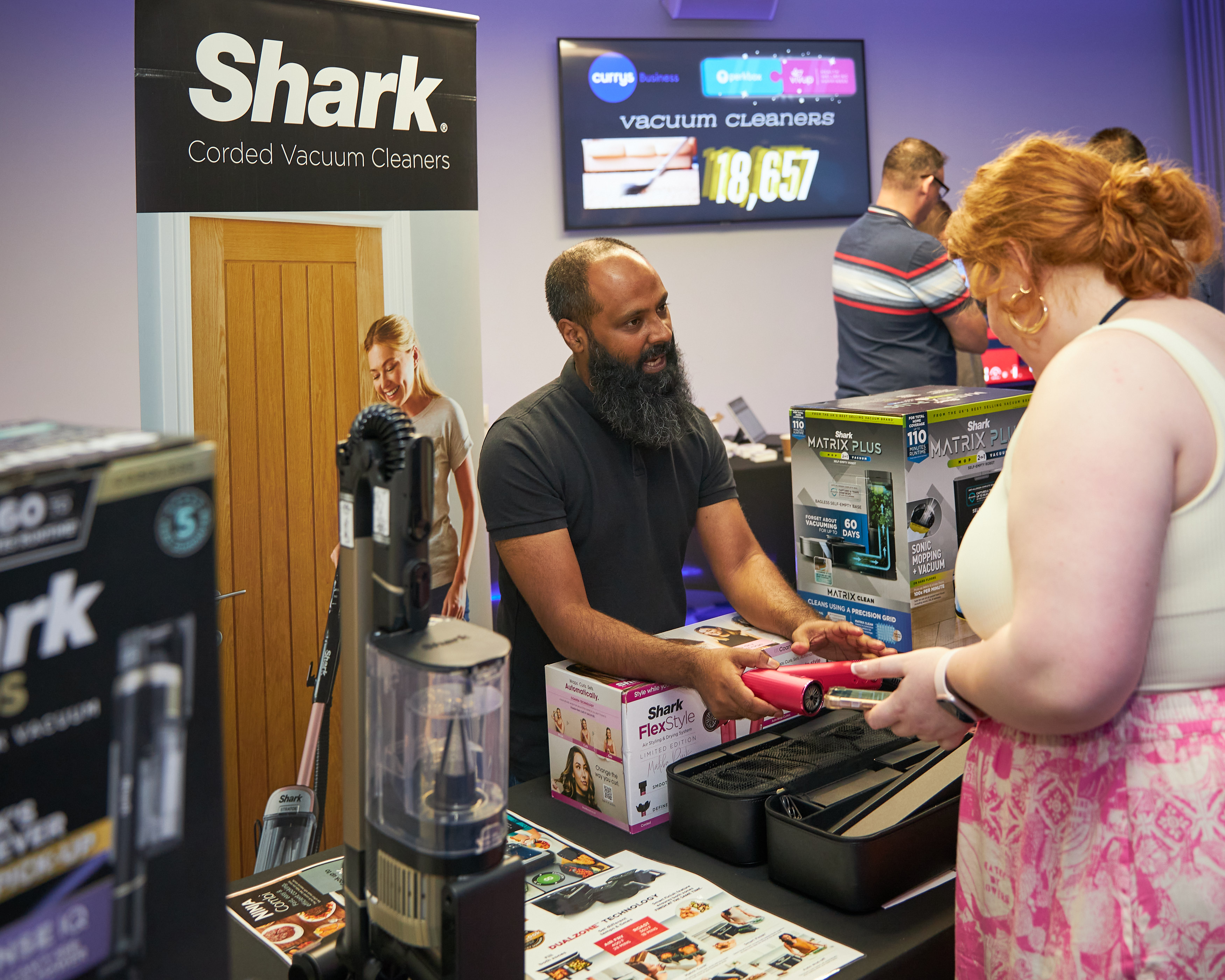 An exhibitor demonstrating a vacuum cleaner to a visitor at a product stand