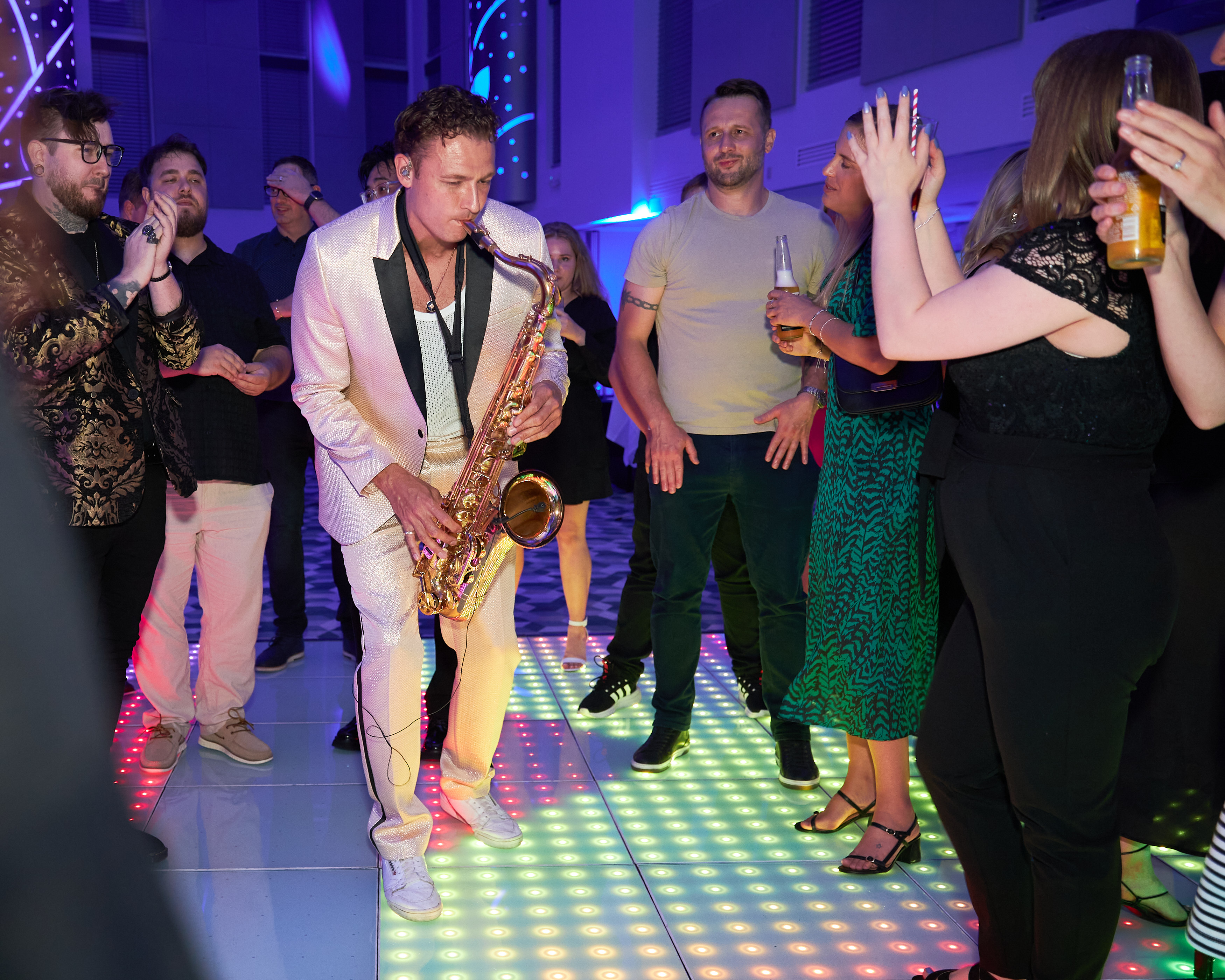 A saxophonist playing on a light-up dance floor surrounded by dancing guests