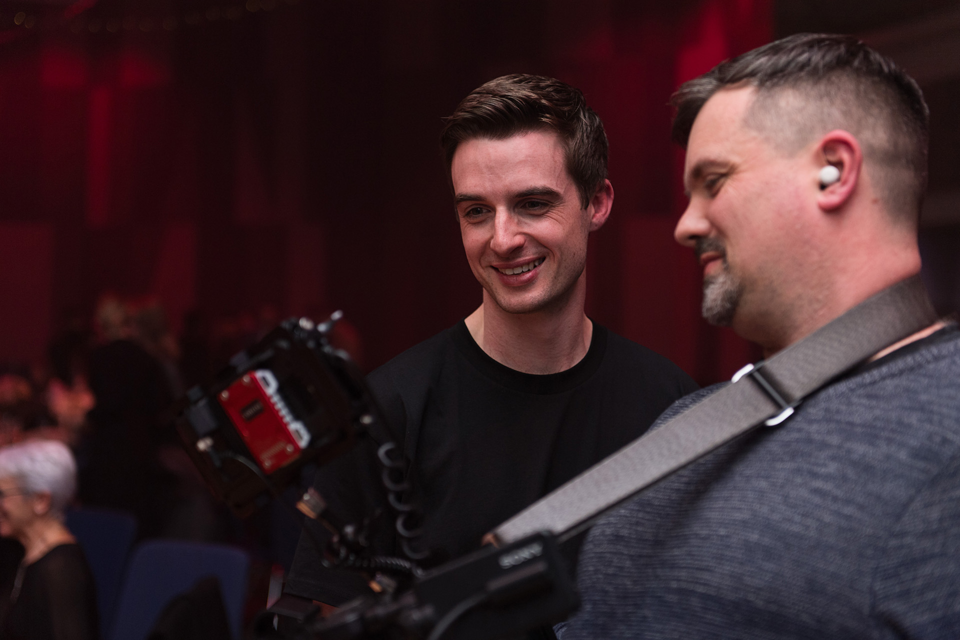 A camera operator filming while talking with a colleague at an event