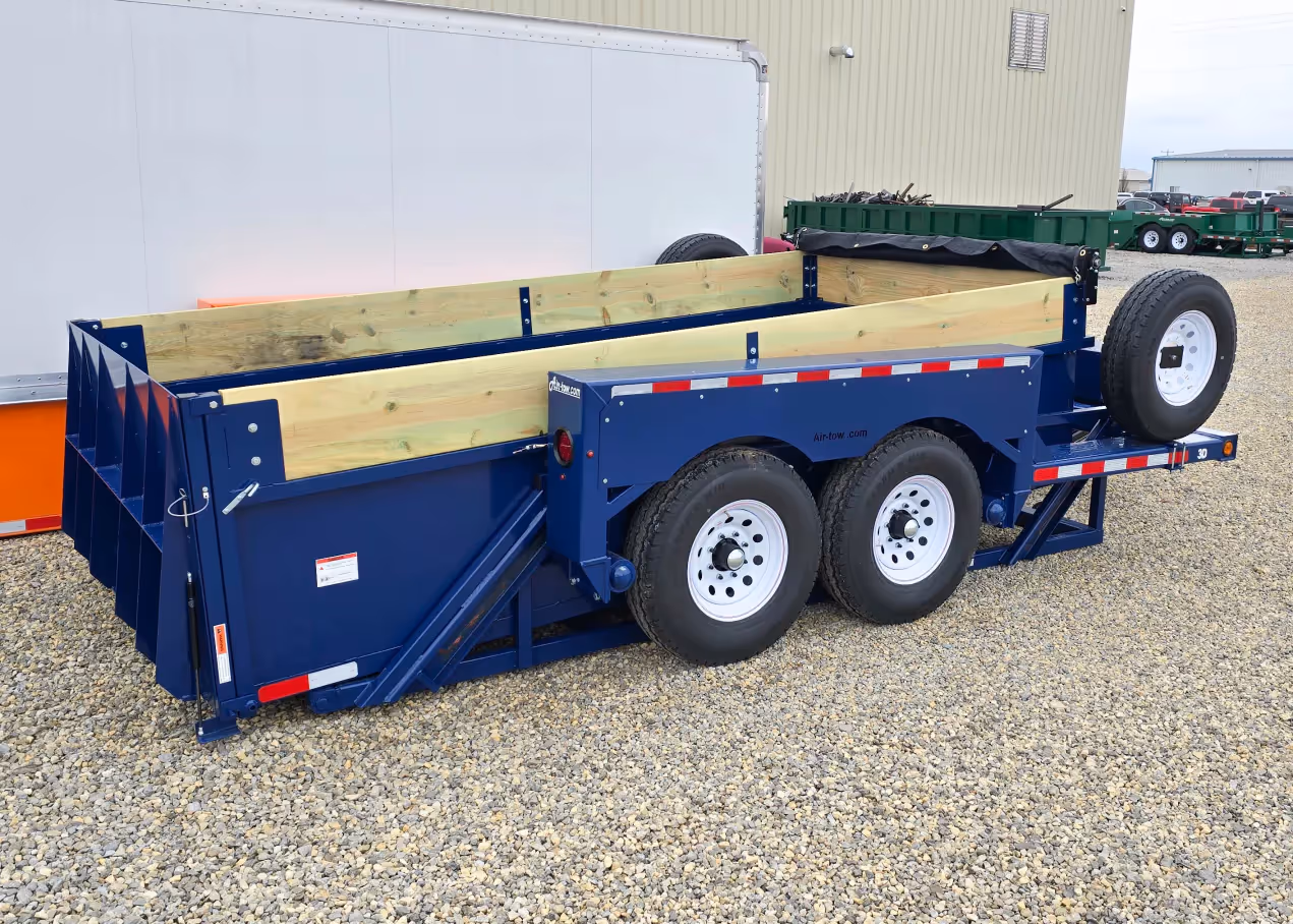 Rear three-quarter view of a blue Air-Tow dump trailer with wood sides and a side-mounted spare tire.