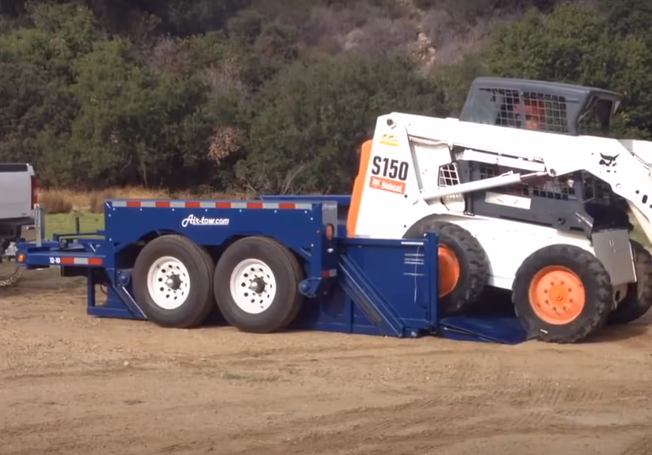 A Bobcat S150 skid steer being driven onto the lowered deck of an Air-Tow trailer, demonstrating the ground-level loading feature.
